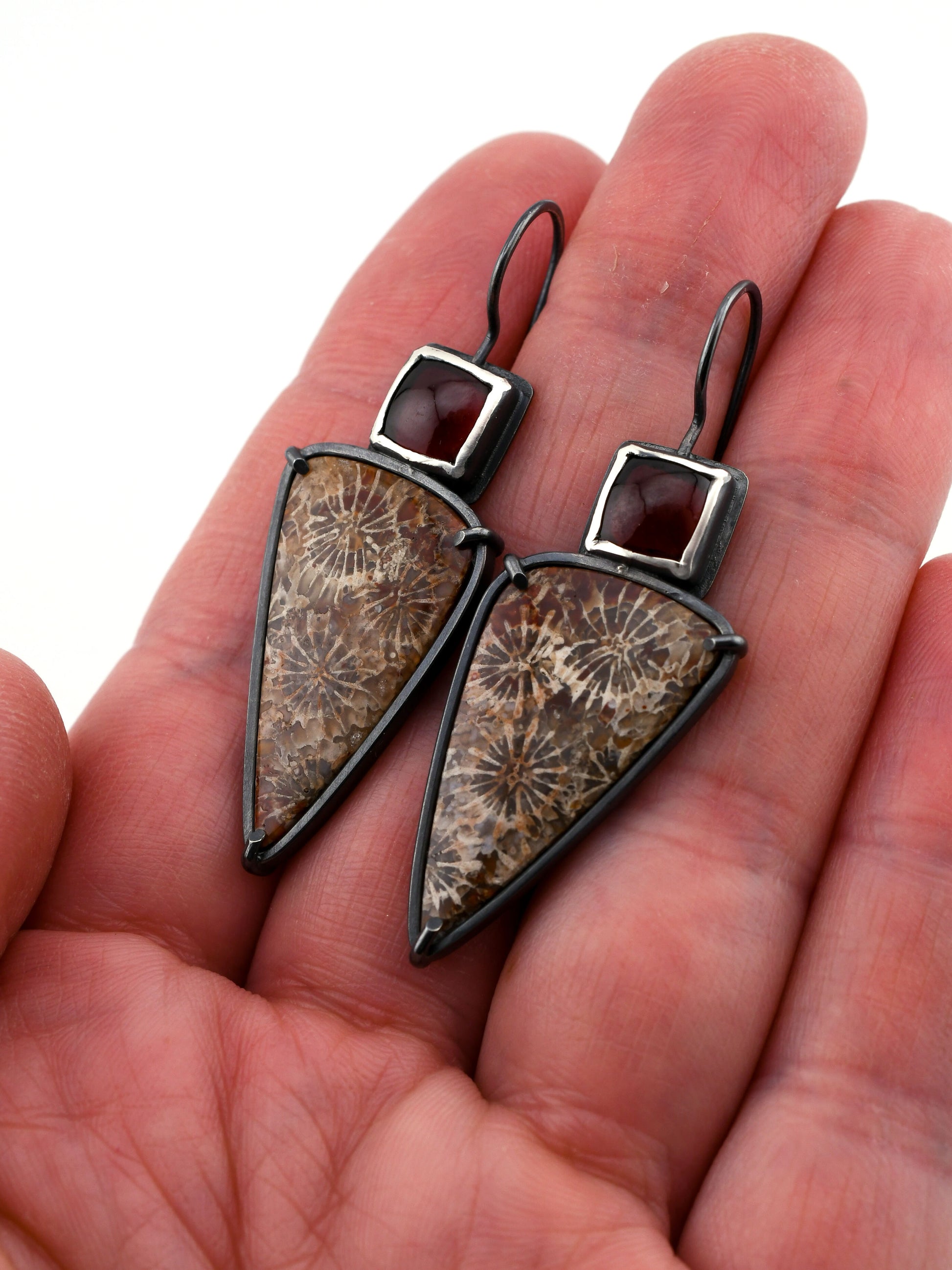Pair of triangular-shaped earrings with brown and silver design held in a hand.