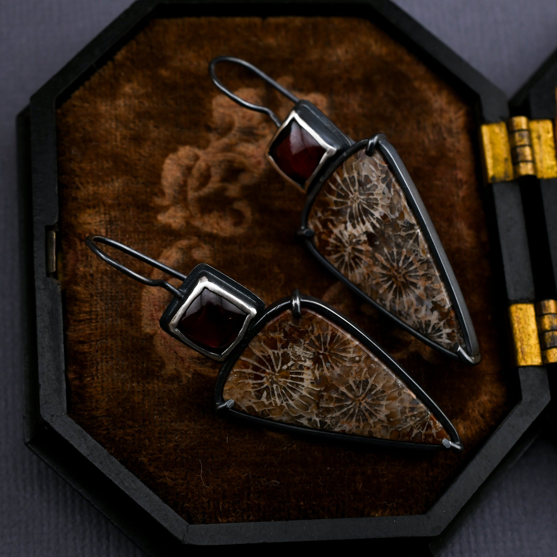 Pair of silver earrings with red gemstones on a textured velvet surface