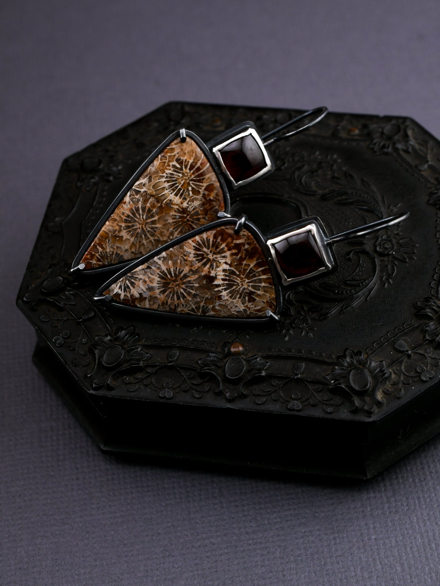 Pair of earrings with triangular brown stones on a dark textured surface