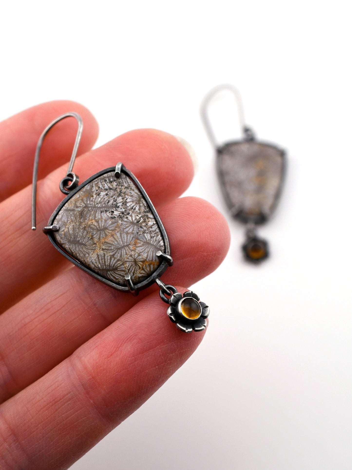 Silver earrings with a textured design held by a hand on a white background