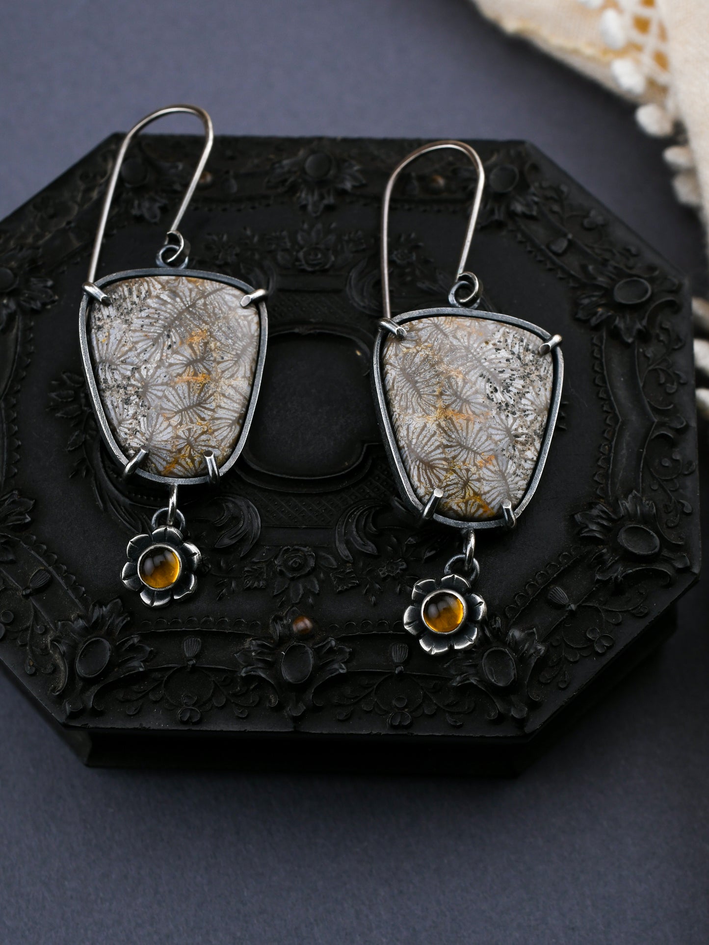 Silver earrings with floral design and amber stones on a dark textured surface