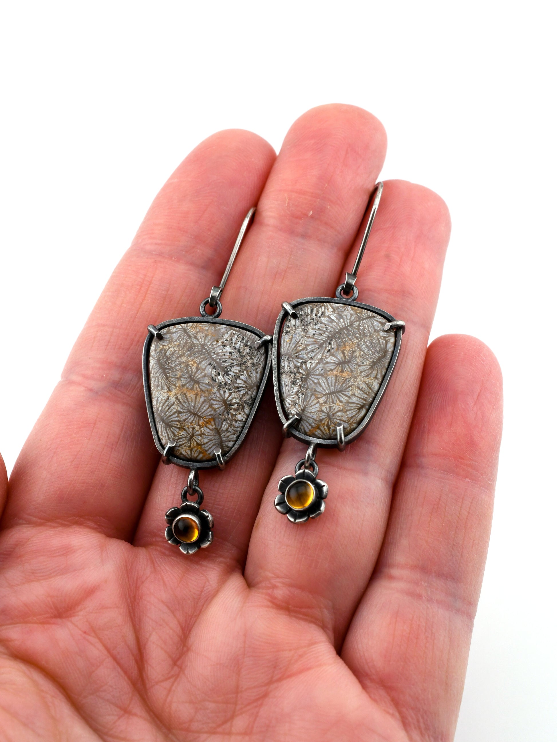 Silver earrings with gemstones held in a hand on a white background