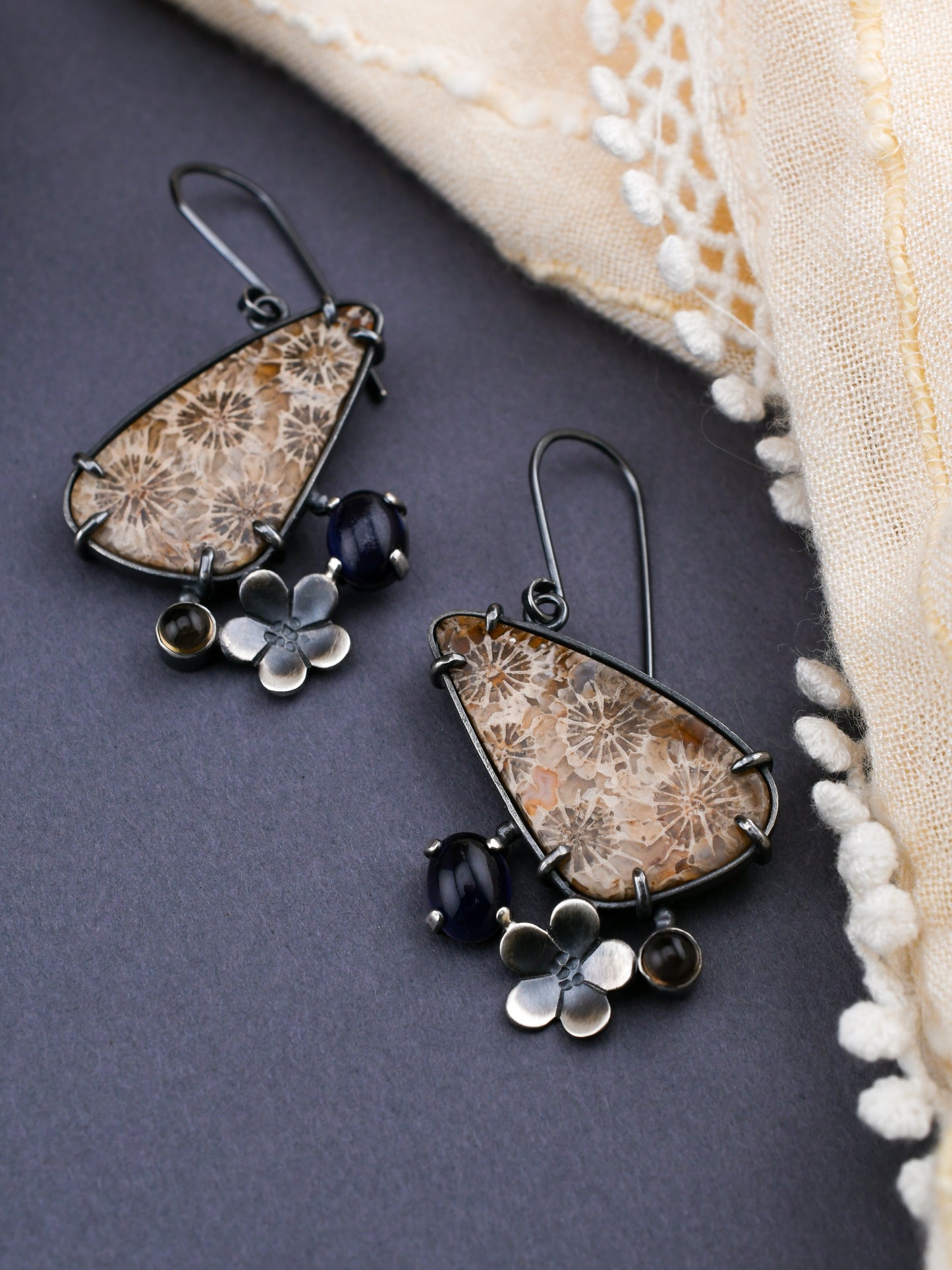 Pair of floral-themed earrings on a dark surface with a beige fabric background