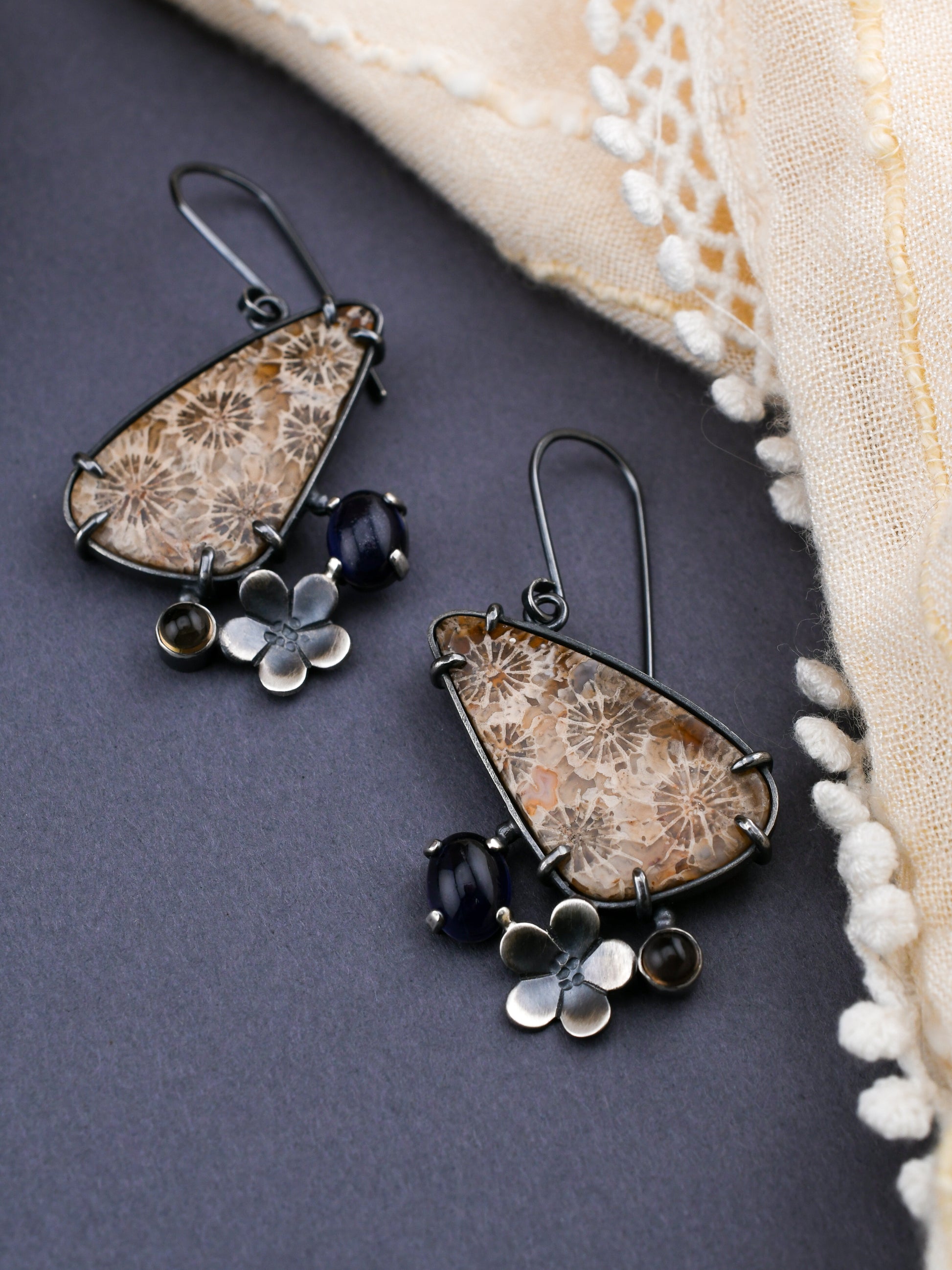 Pair of floral-themed earrings on a dark surface with a beige fabric background