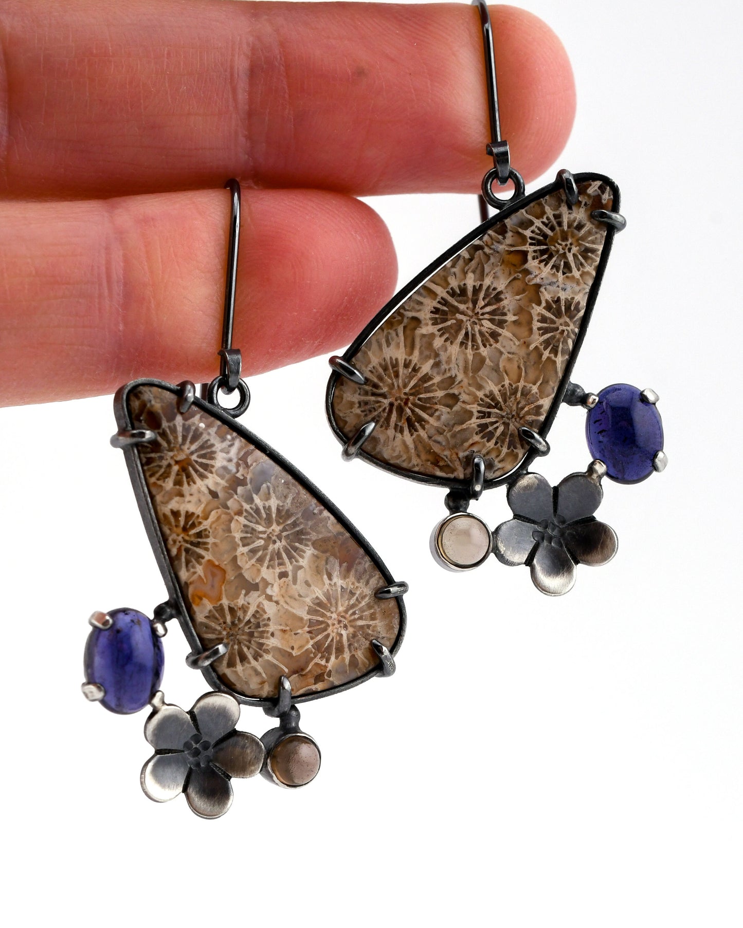 Pair of earrings with floral and blue stone designs held between fingers.