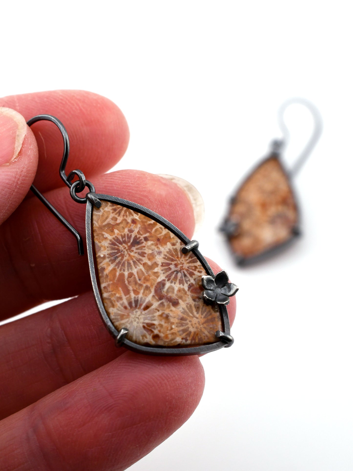 Fossilized coral earring held between fingers with a matching earring in the background.
