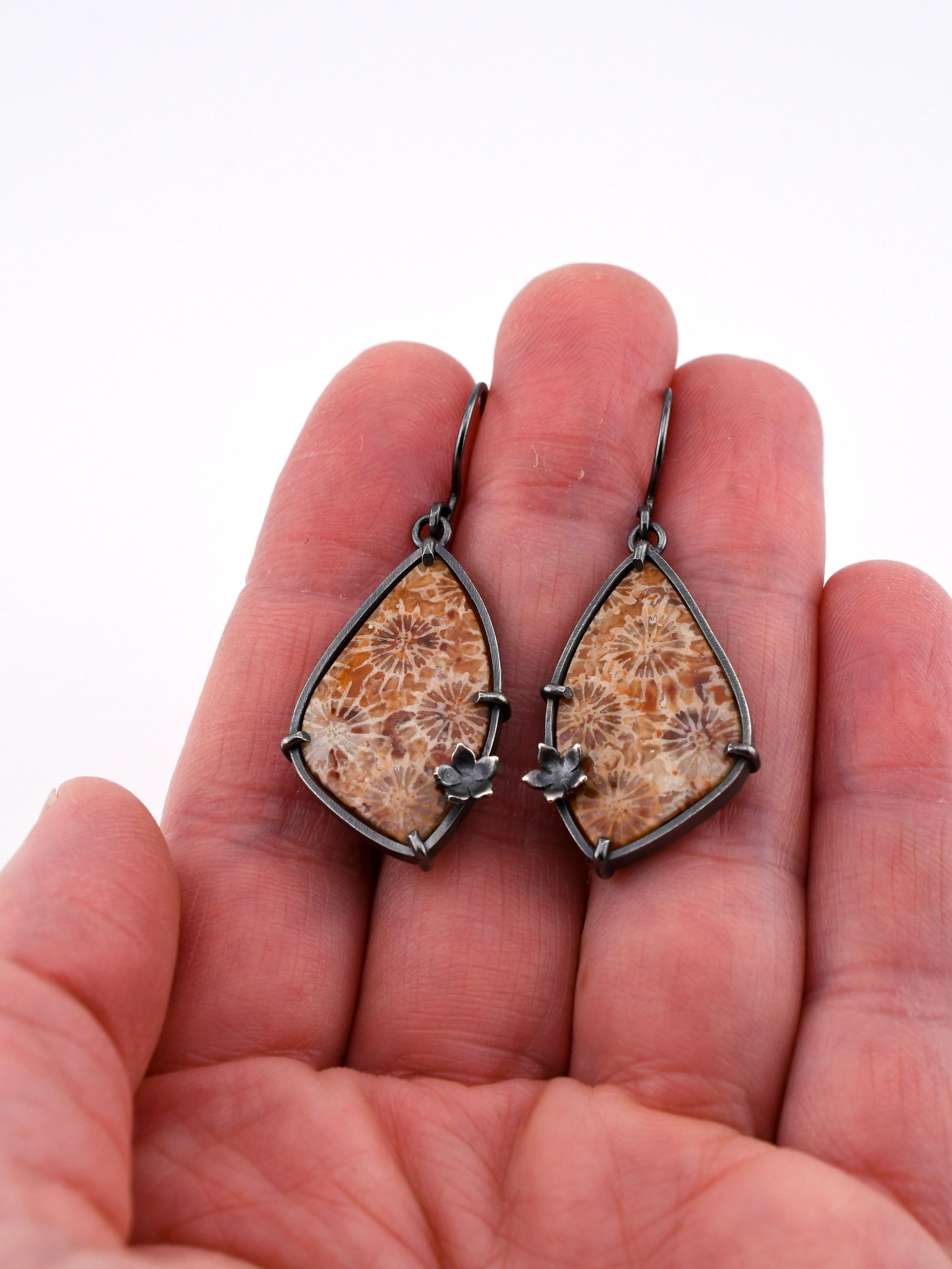 Wing-shaped earrings with natural stone design held between fingers on a white background