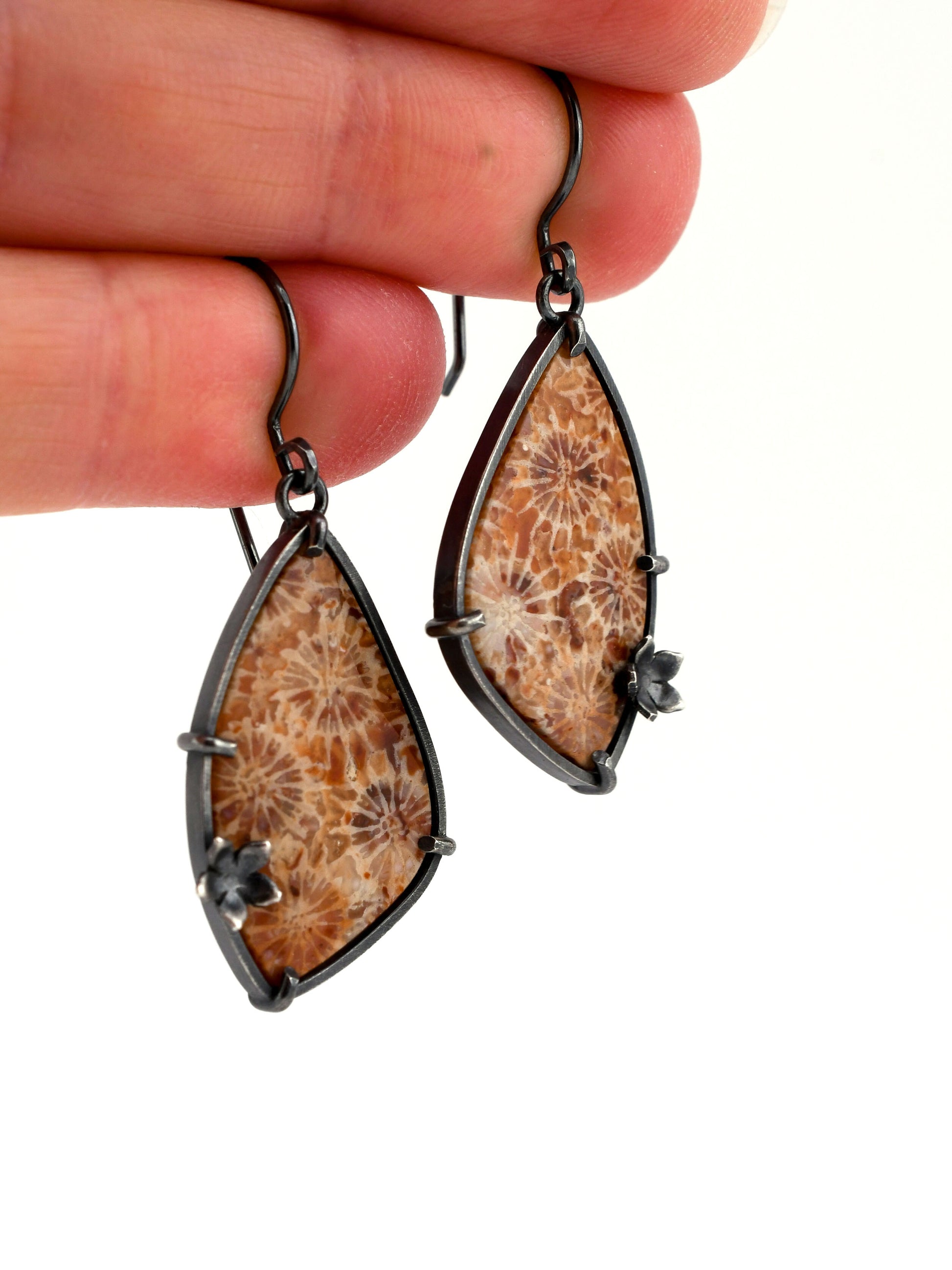 Wing-shaped earrings with natural design held by a hand on a white background