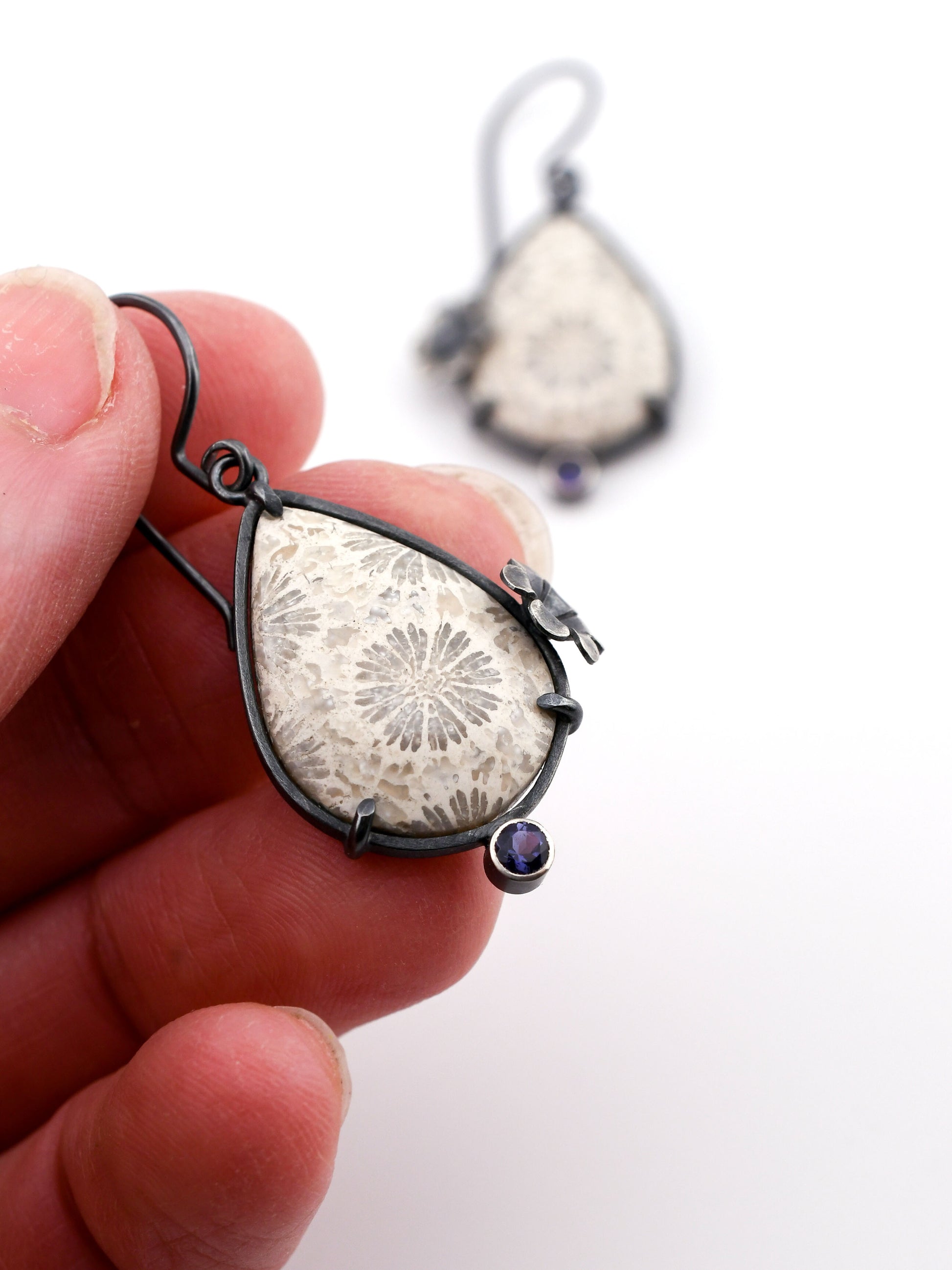 Teardrop-shaped silver earring with a floral design held by a hand against a white background.