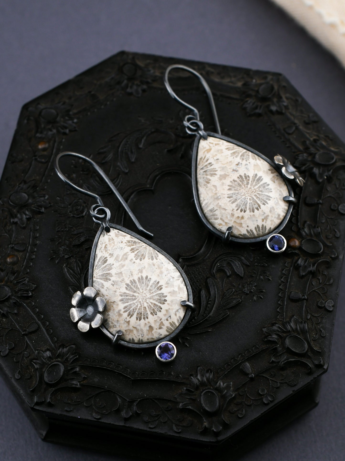 Teardrop-shaped earrings with floral and gemstone details on a dark decorative background