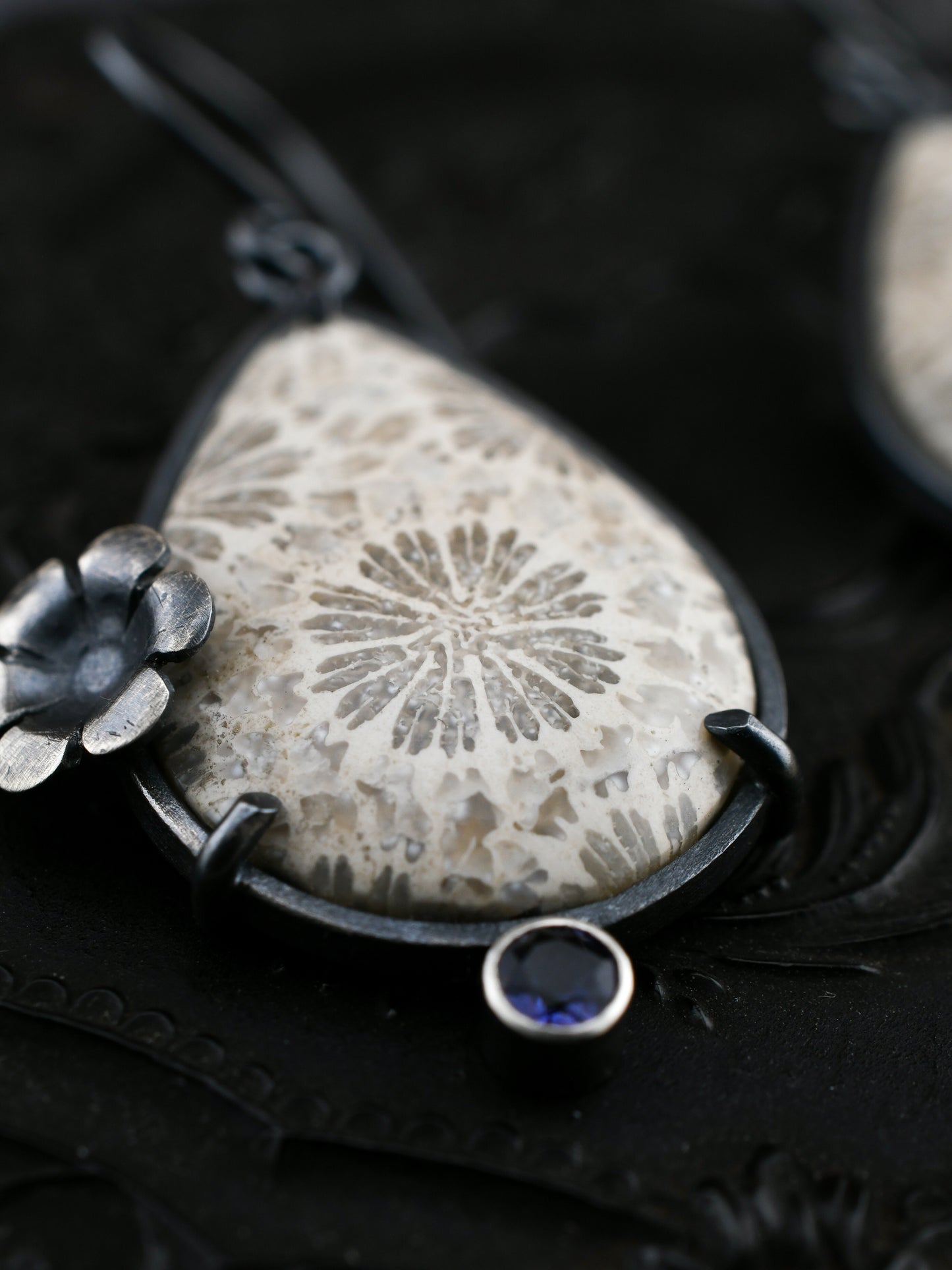 Earring with a teardrop-shaped fossil coral and floral design on a dark background