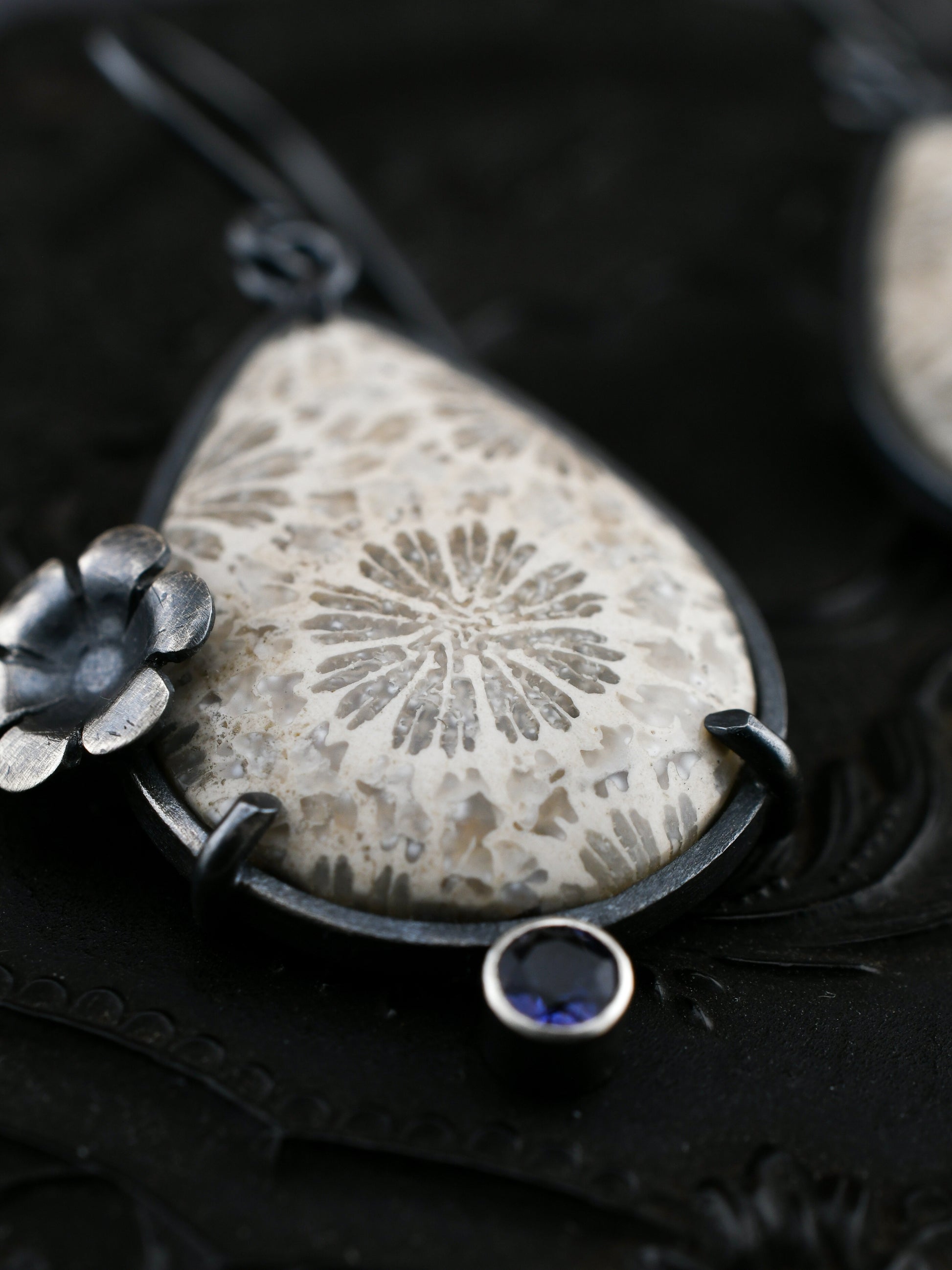 Earring with a teardrop-shaped fossil coral and floral design on a dark background