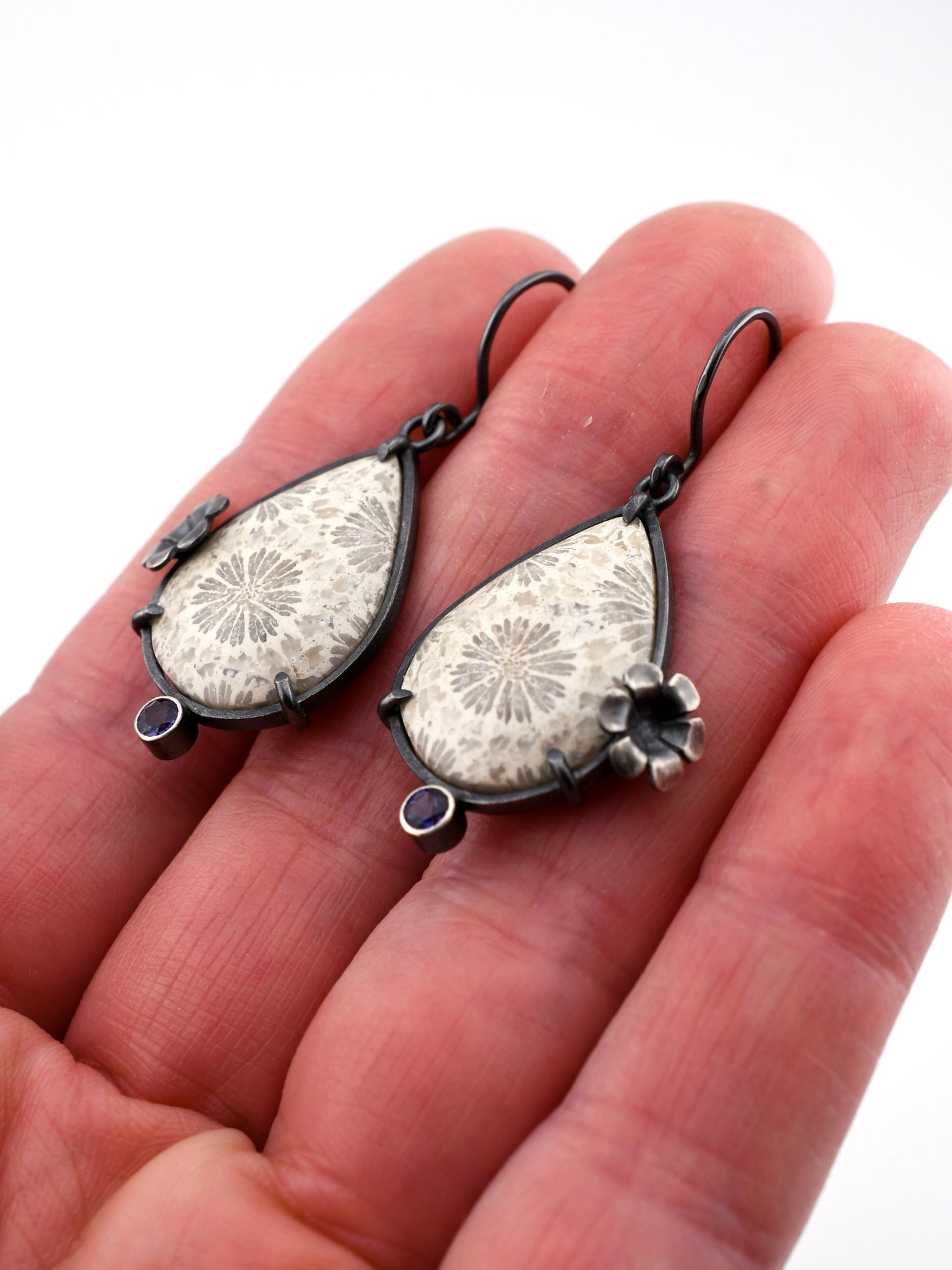 Teardrop-shaped earrings with floral design held between fingers on a white background