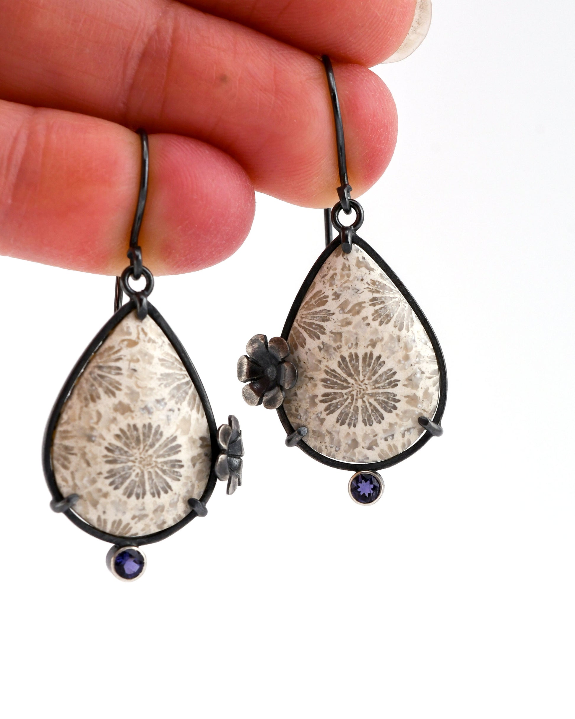 Teardrop-shaped earrings with floral designs held between fingers on a white background