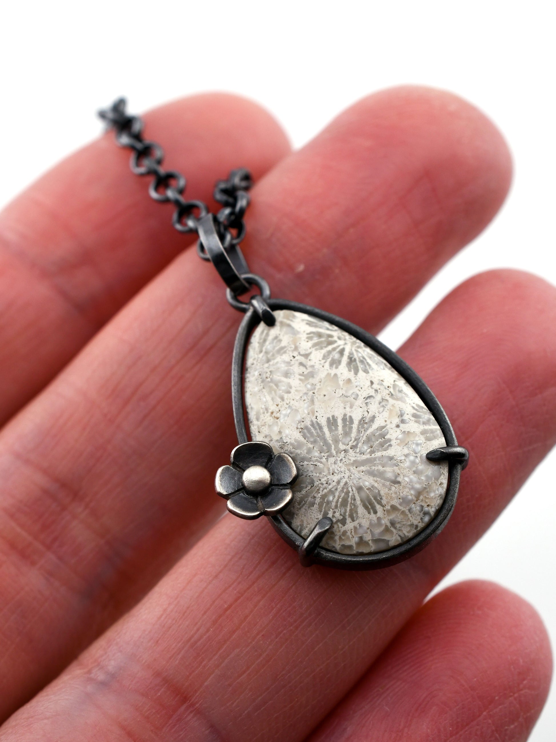 Silver necklace with a floral pendant held between fingers on a white background