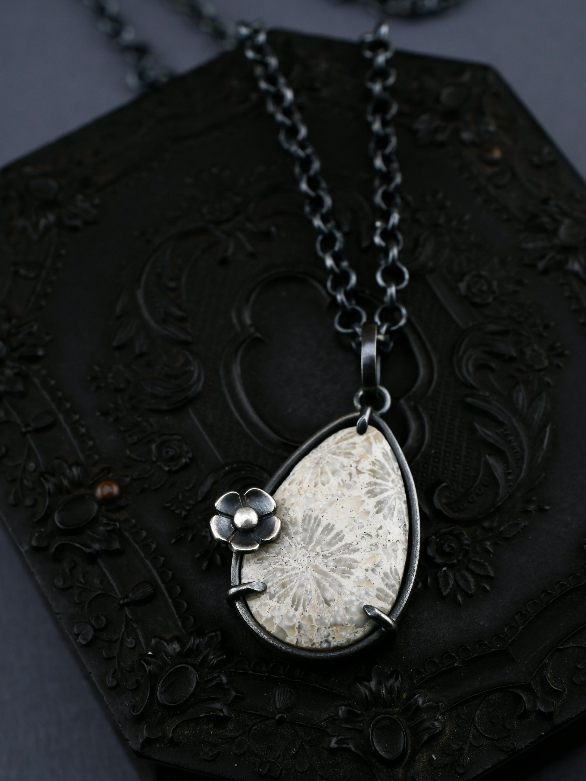 Teardrop necklace with white fossil coral and flower details on a decorative black background