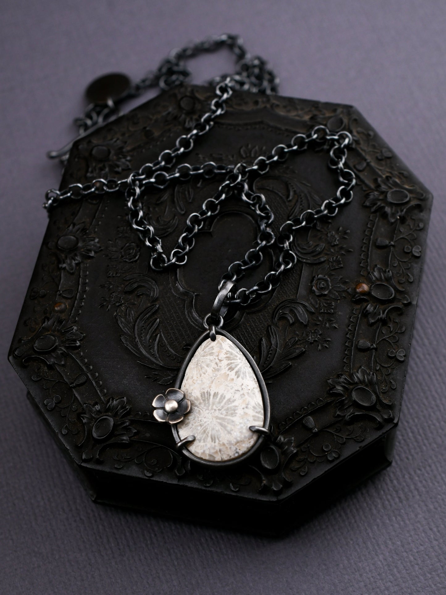 Black ornate box with a chain and teardrop pendant on a dark background