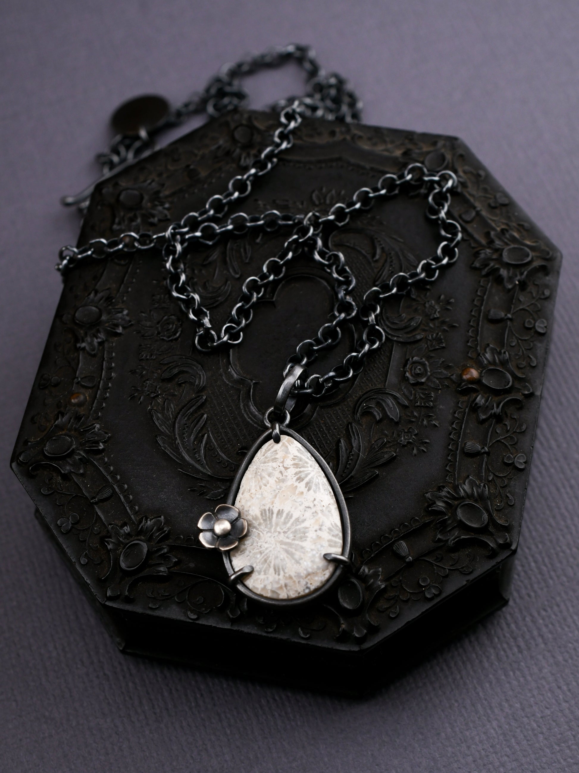Black ornate box with a chain and teardrop pendant on a dark background
