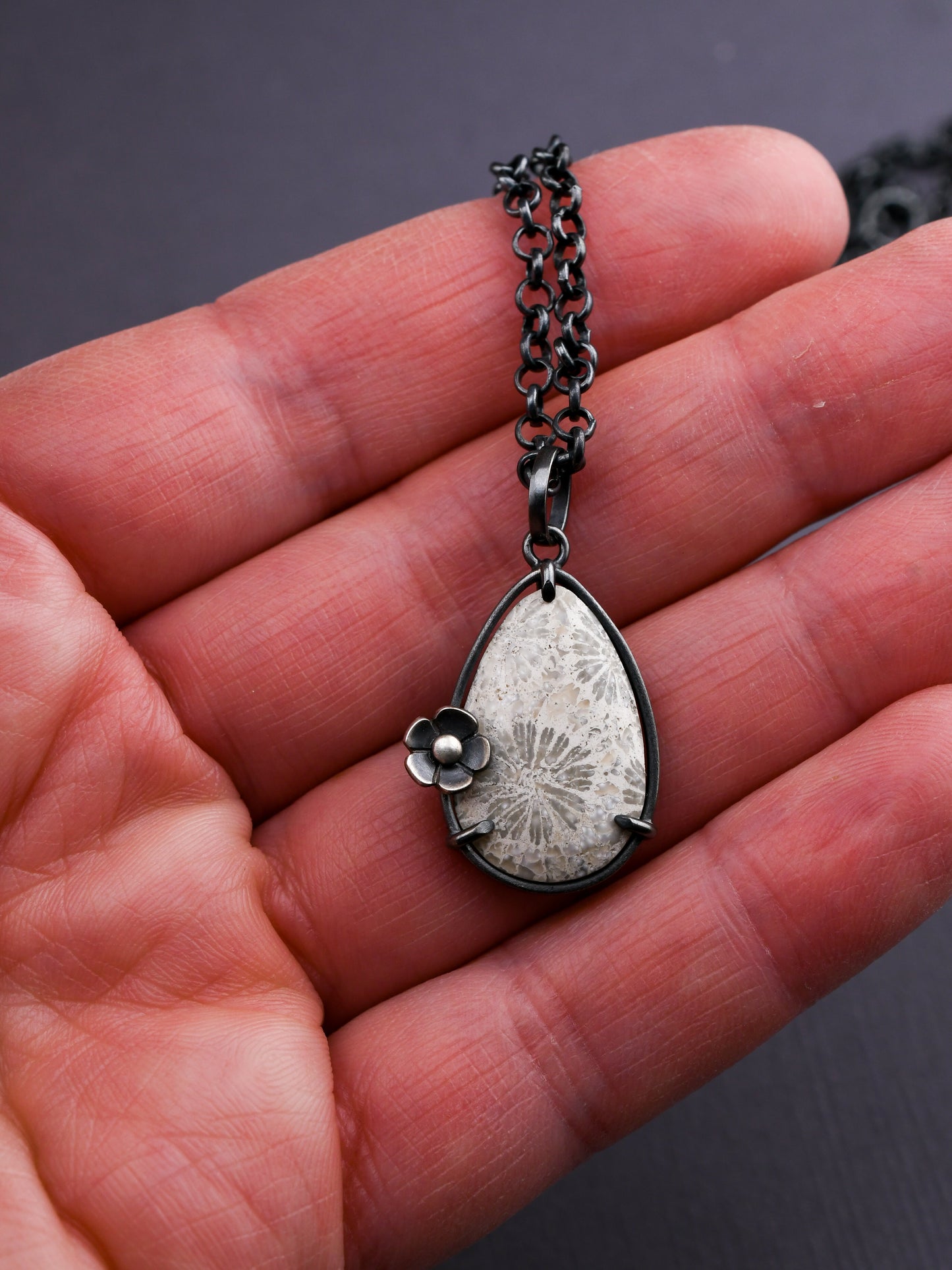 Silver necklace with a teardrop-shaped pendant held in a hand against a dark background