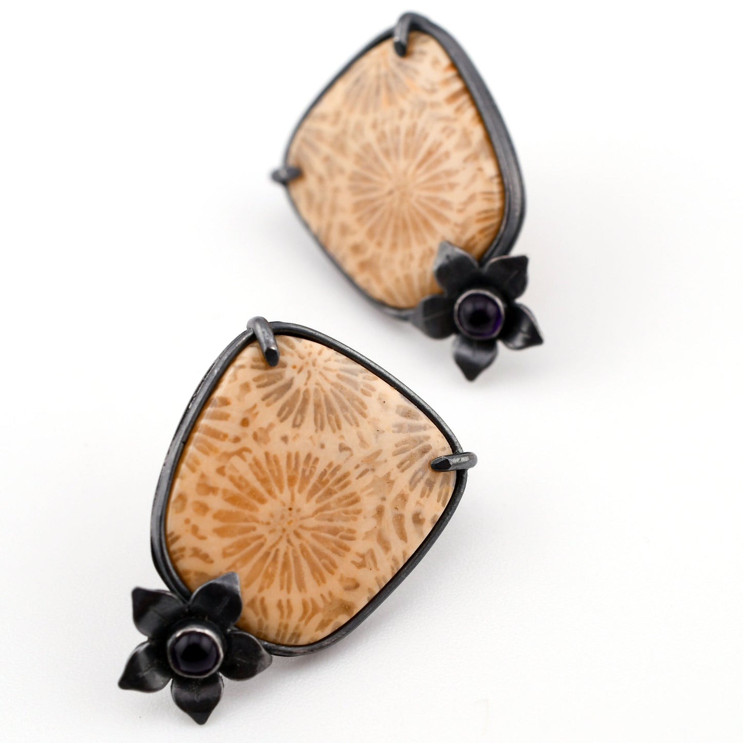 Pair of earrings with fossil coral stones and black floral accents on a white background