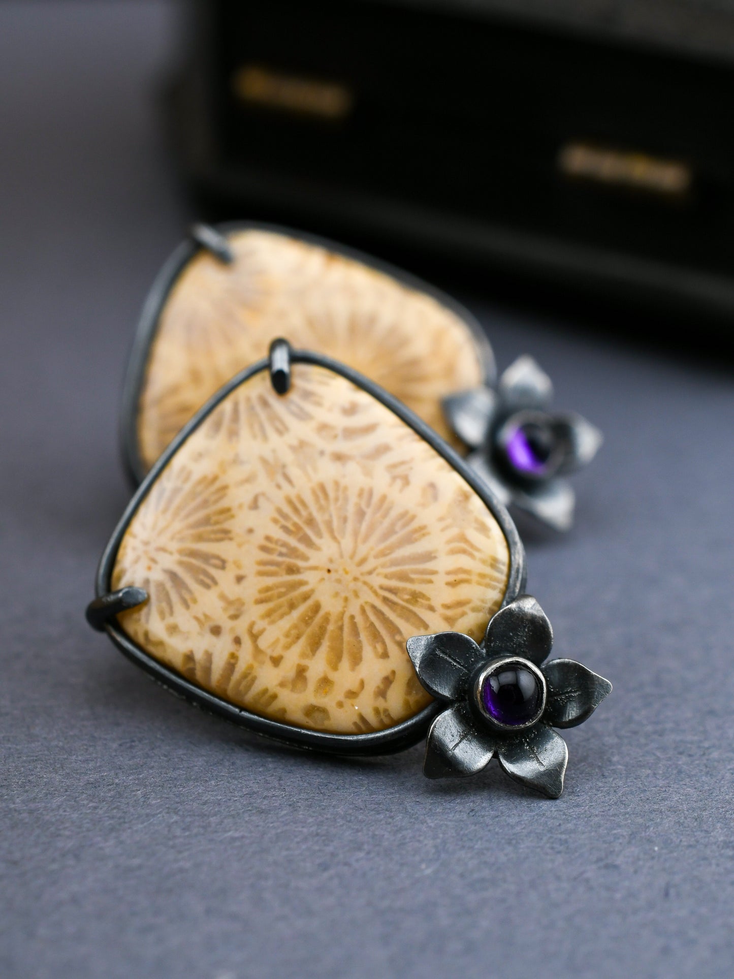 Pair of earrings with floral designs and purple gemstones on a dark surface