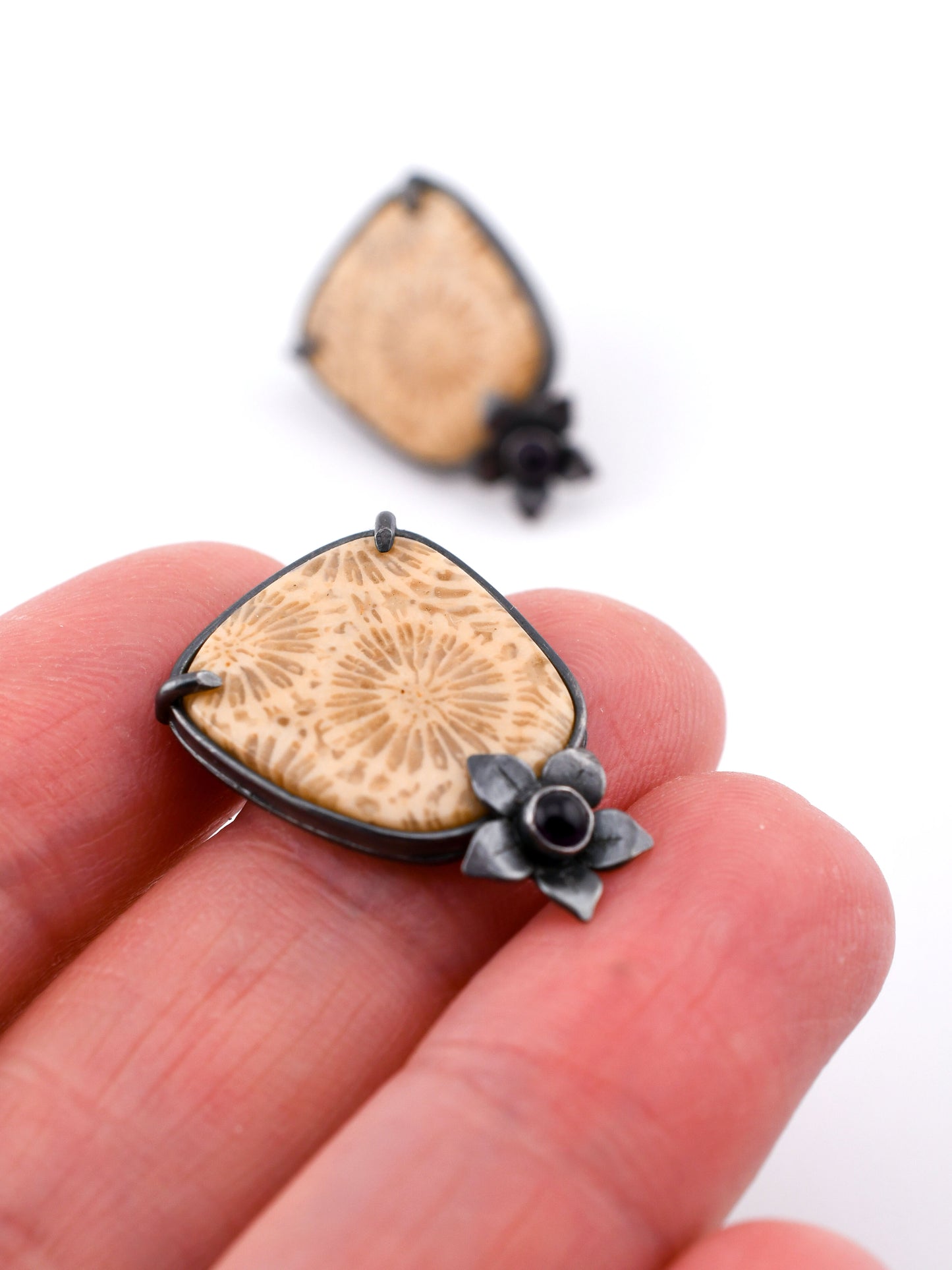 Coral earrings held between fingers with a white background