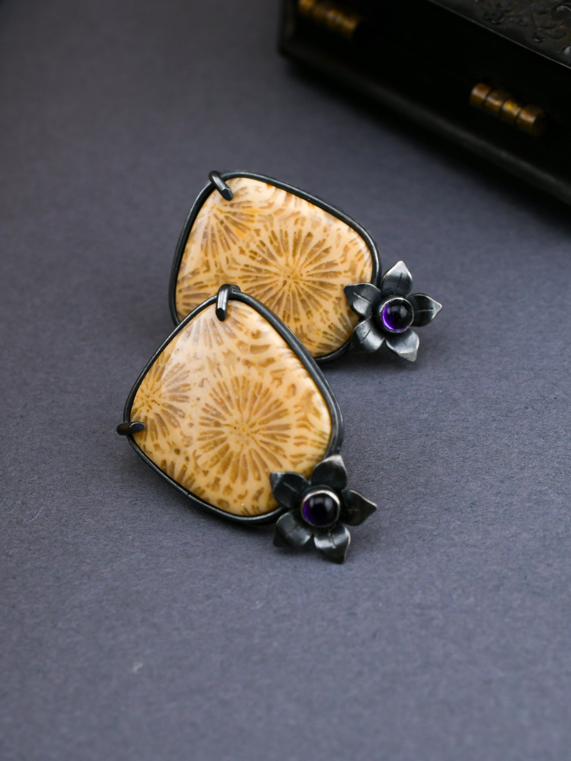 Pair of earrings with fossilized coral and floral designs on a dark background