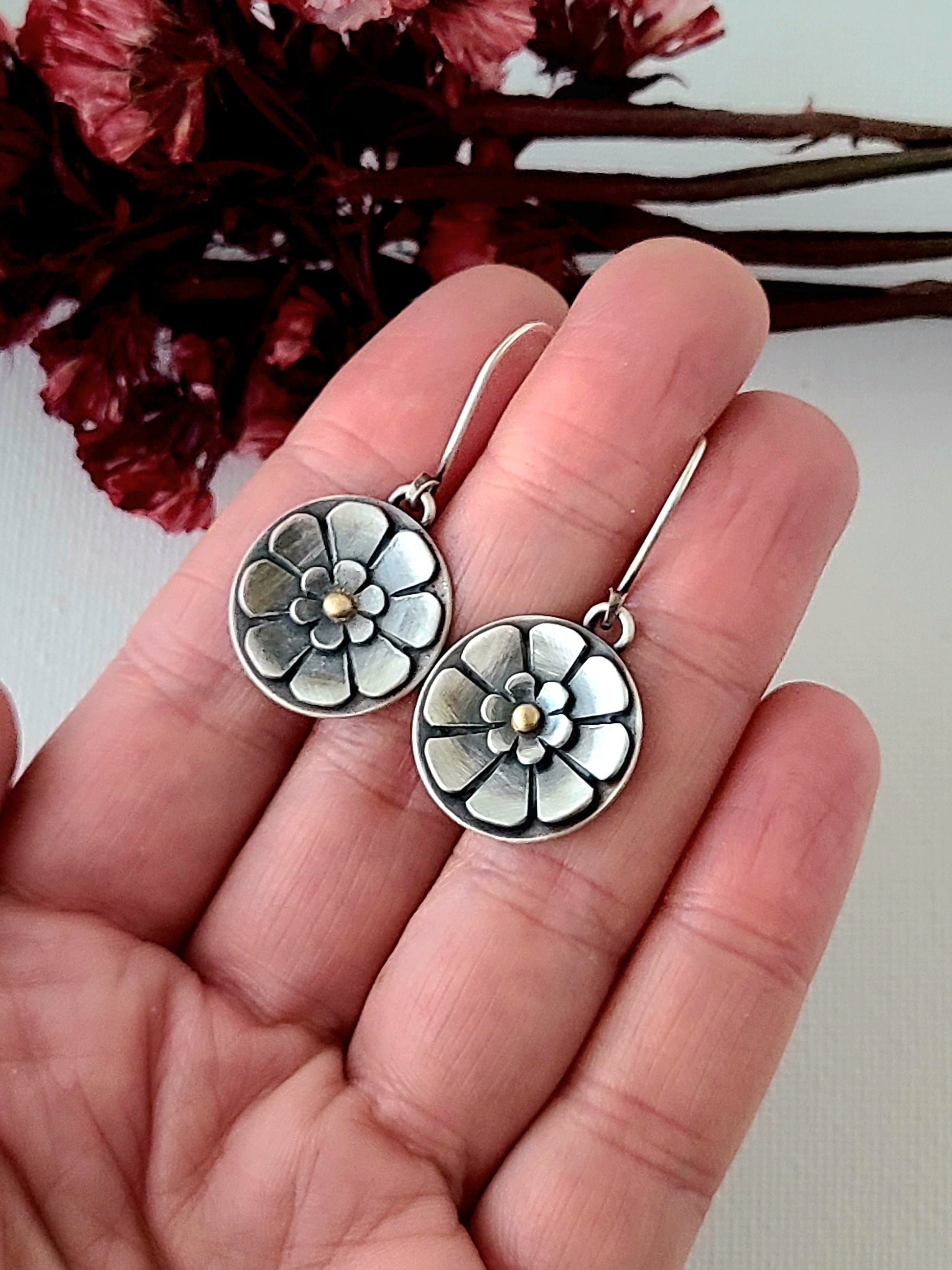 Flower earrings held in a hand on  white background with red dried flowers