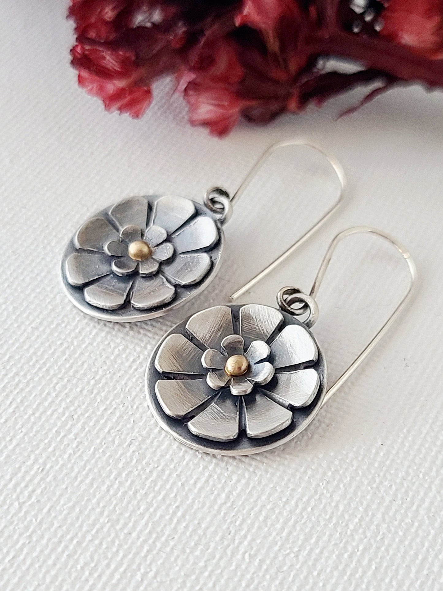 pair of flower earrings with gold centers on a white background with red dried flowers