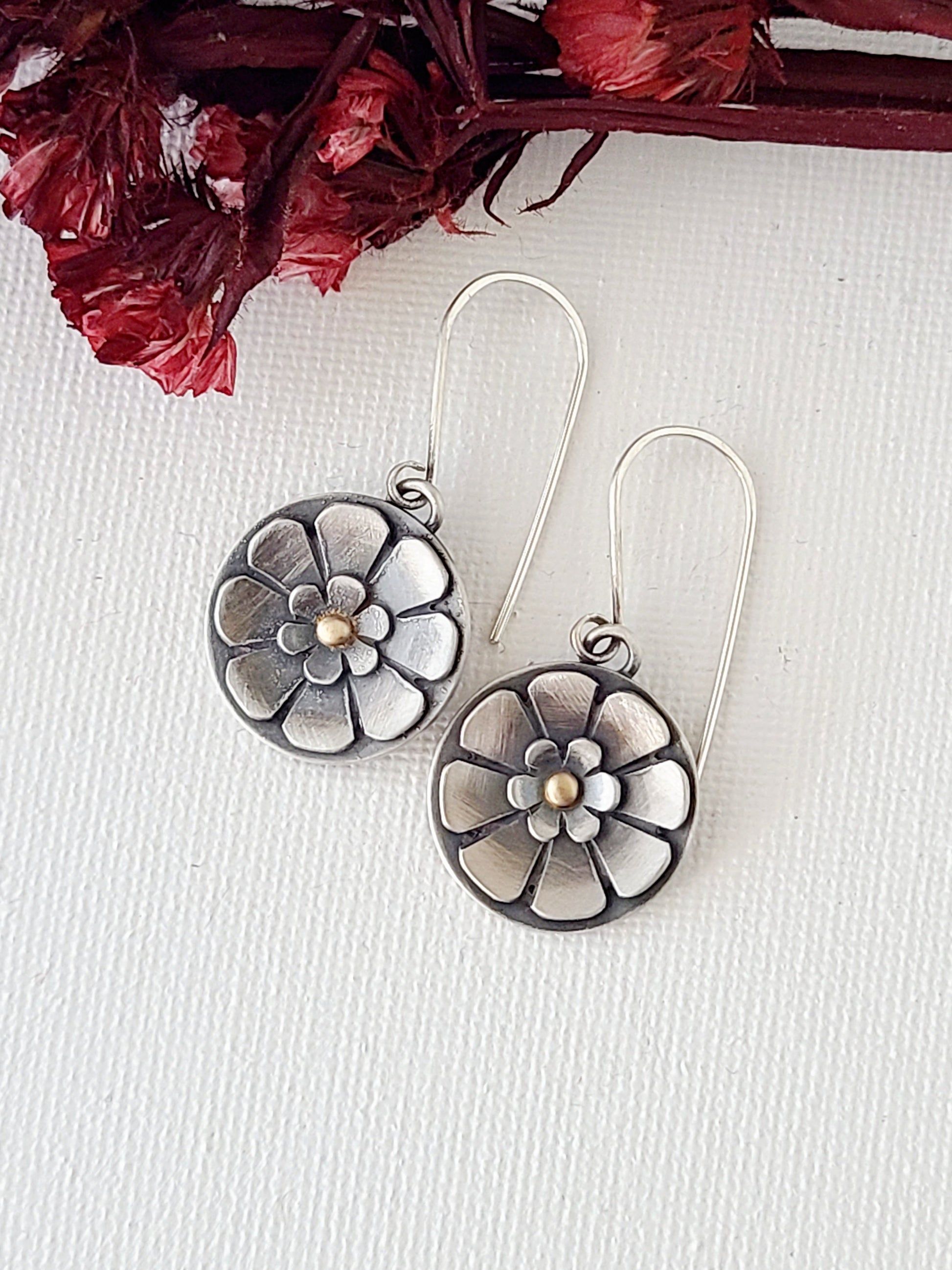 Pair of flower earrings with gold centers with dried red flowers and a textured white background