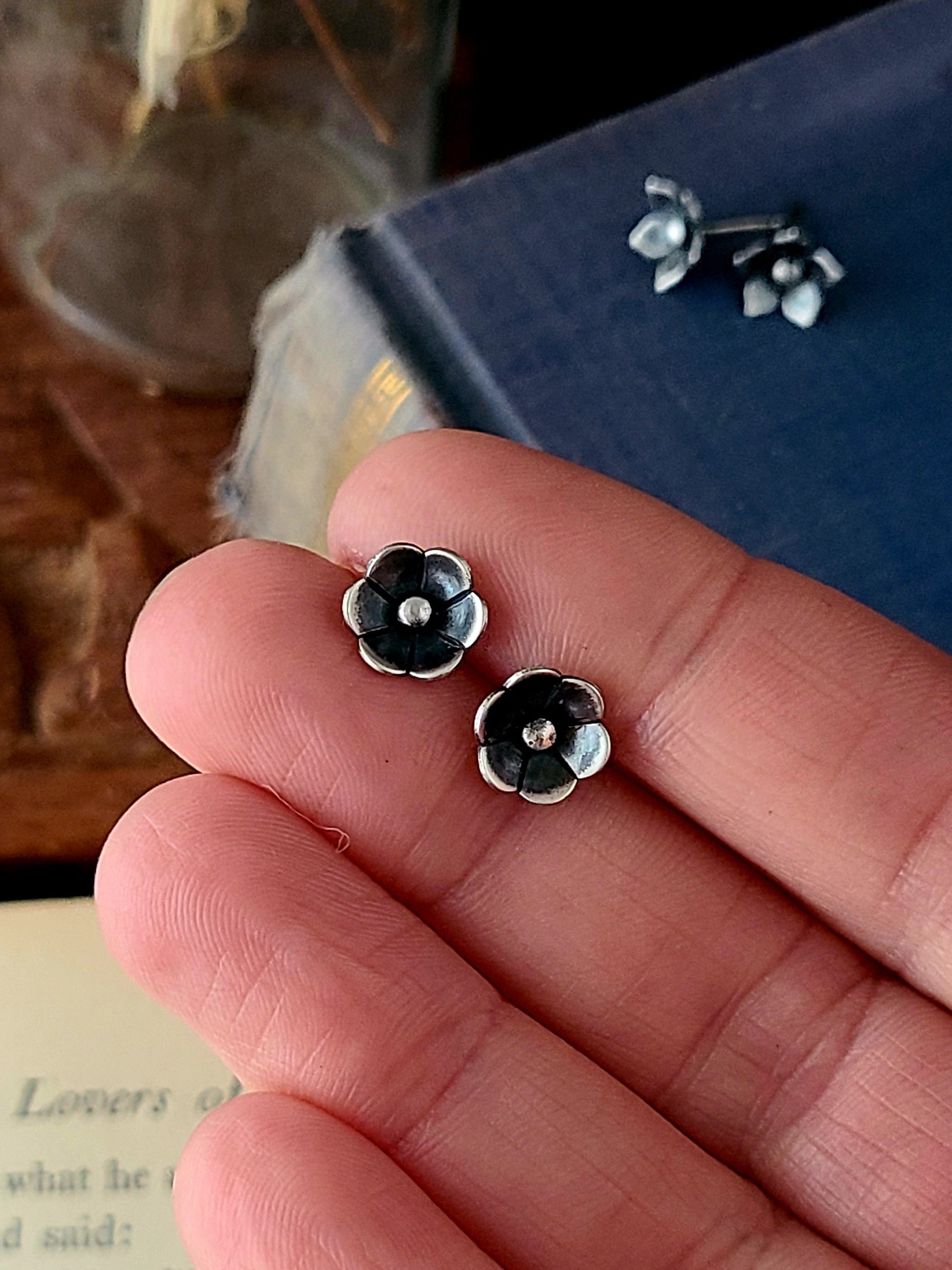 silver flower studs with six petals held in a hand over an open book and a wood box