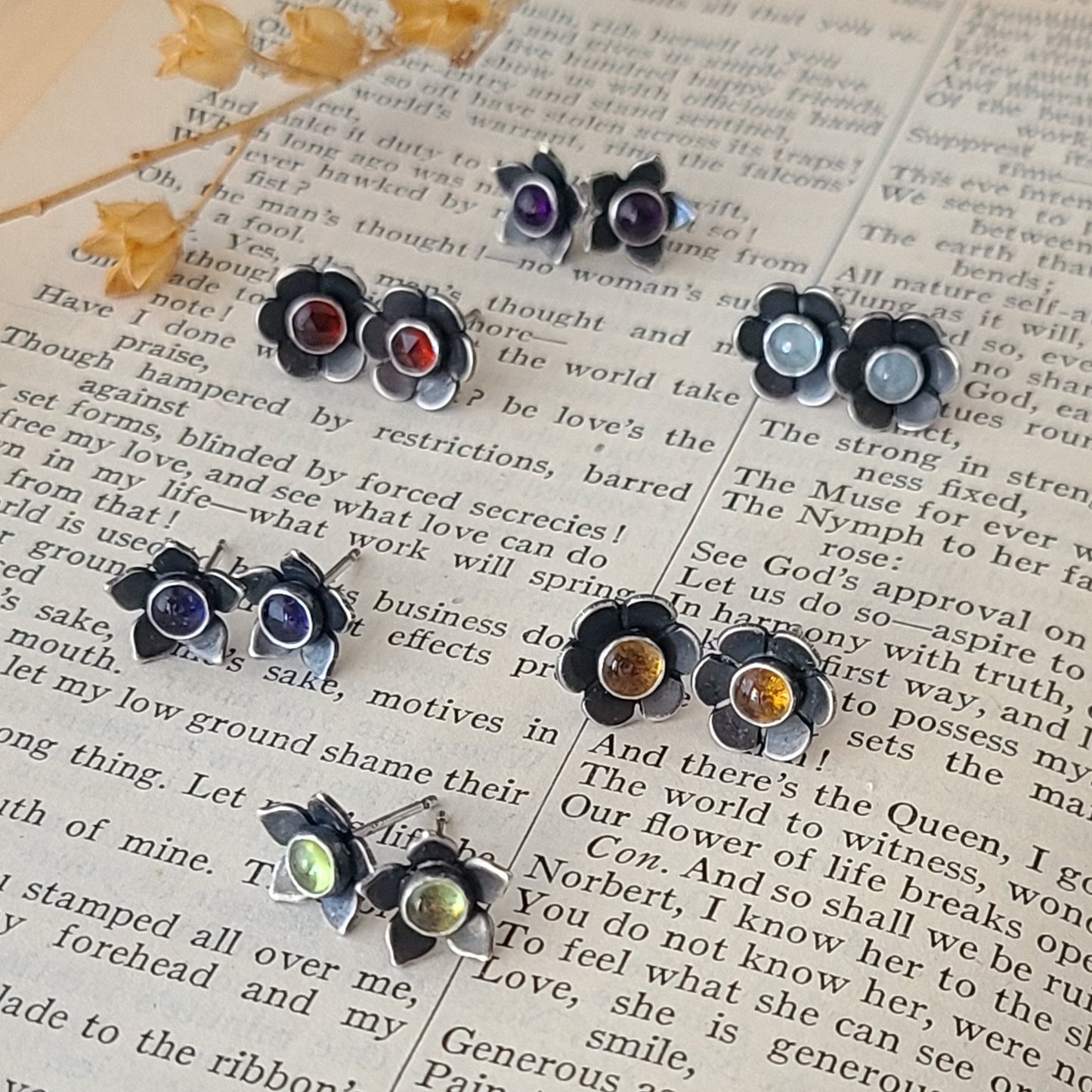 Handcrafted sterling silver flower studs with various gemstones displayed on an open book.