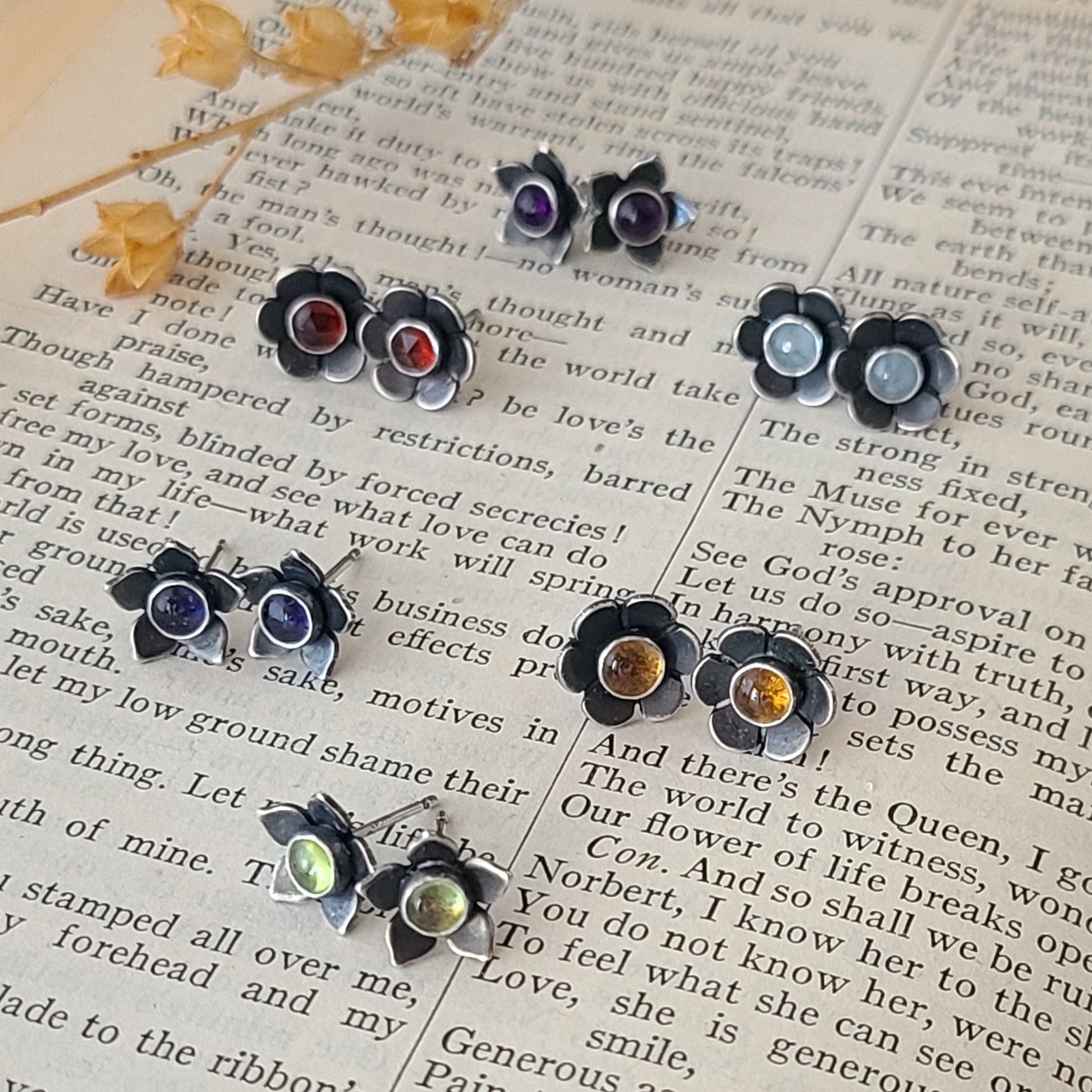 Handcrafted sterling silver flower studs with various gemstones displayed on an open book.