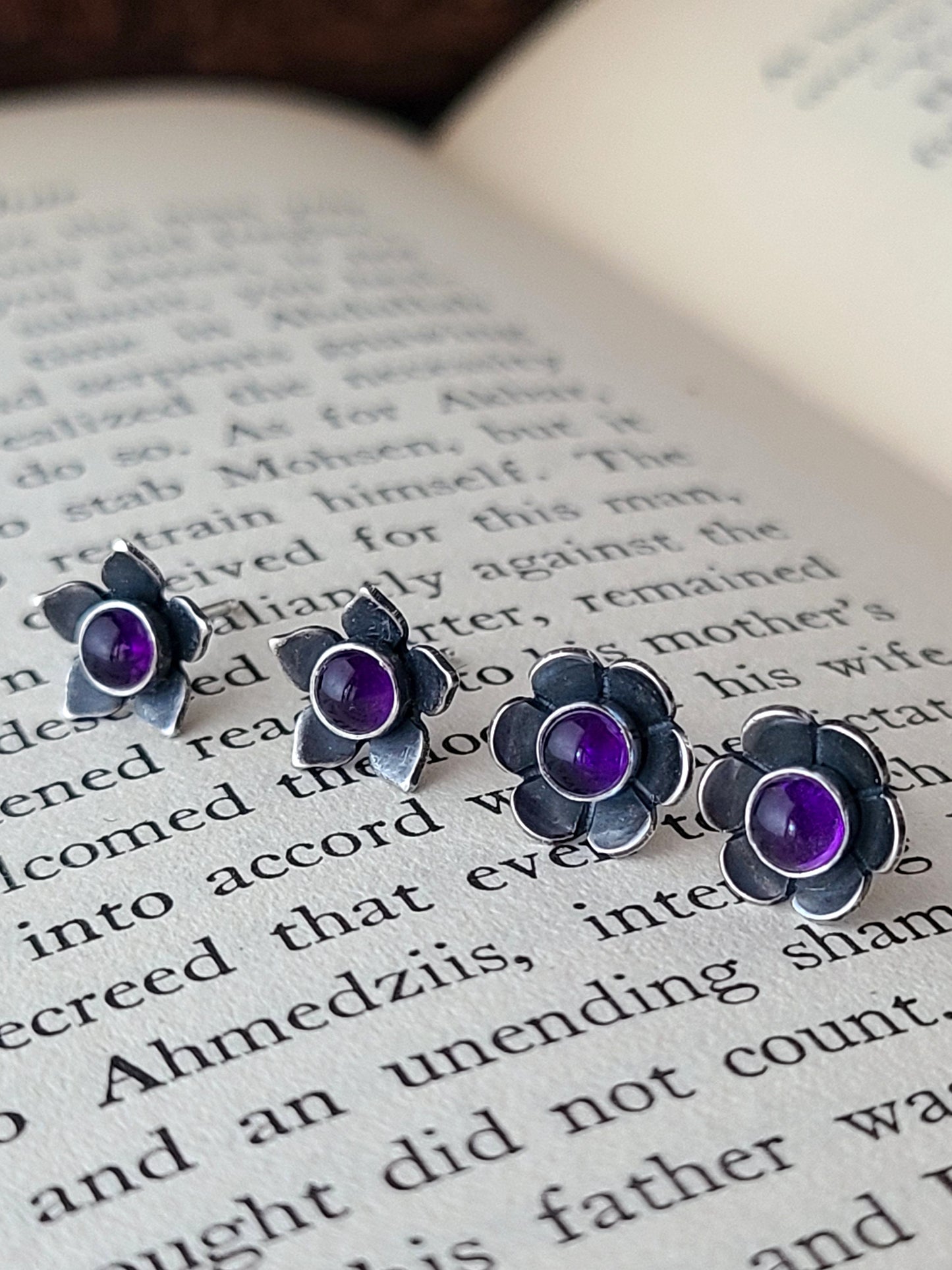 two pairs of flower stud earrings with purple gemstone centers displayed on an open book