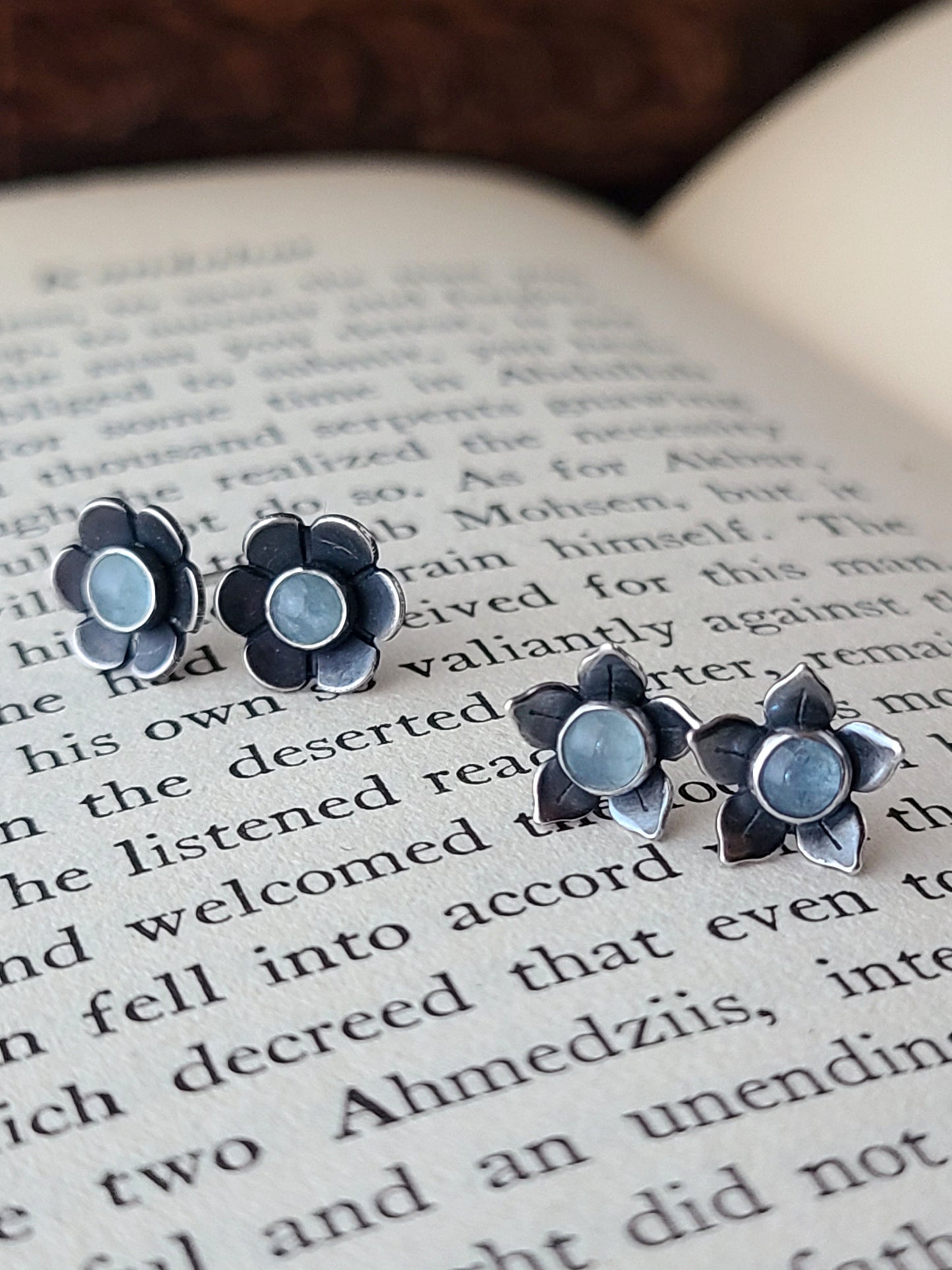 Flower stud earrings with blue gemstones displayed on an open book