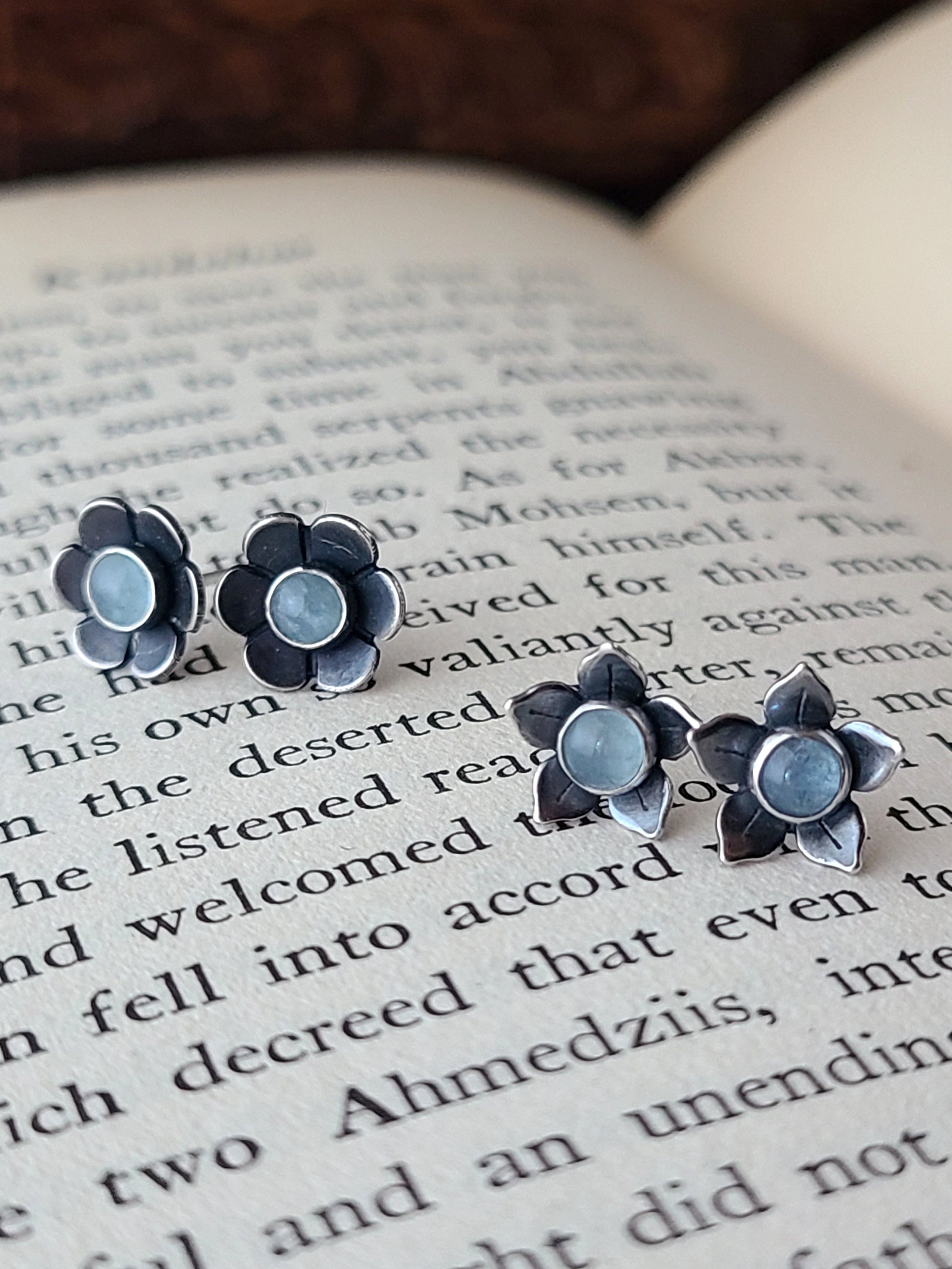Flower stud earrings with blue gemstones displayed on an open book