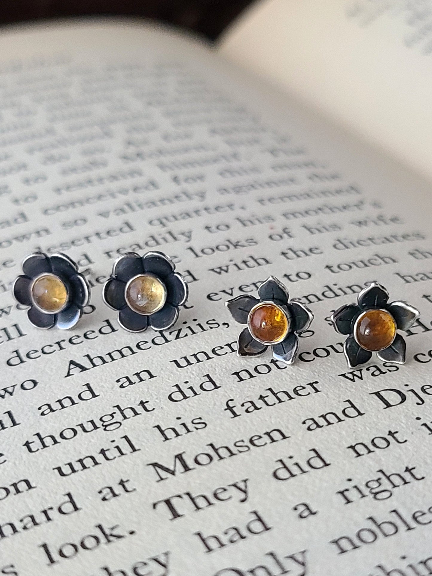 Two pairs of silver flower stud earrings with yellow gemstones displayed on an open book