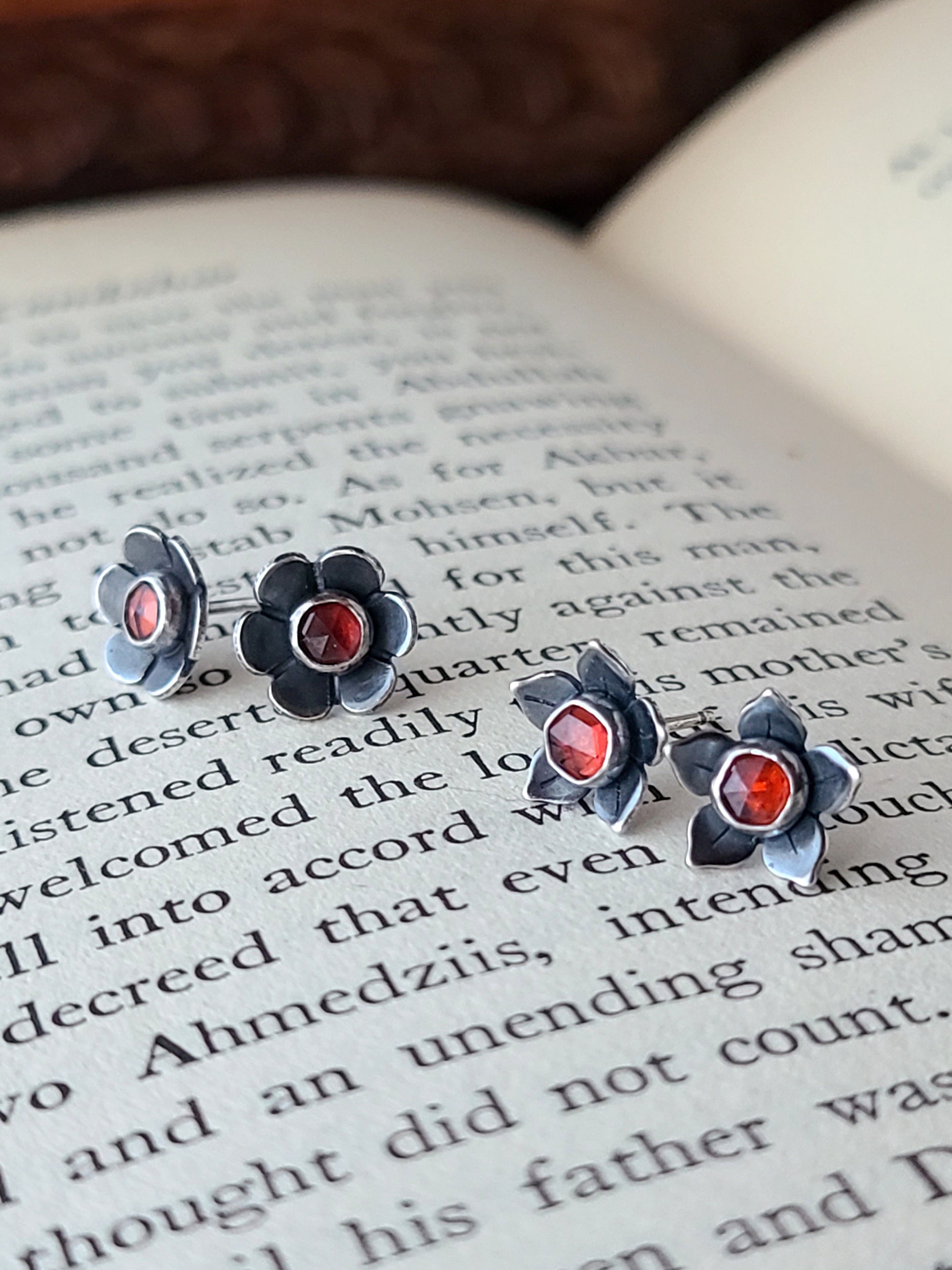 two pairs of silver flower studs with red gemstones displayed on an open book