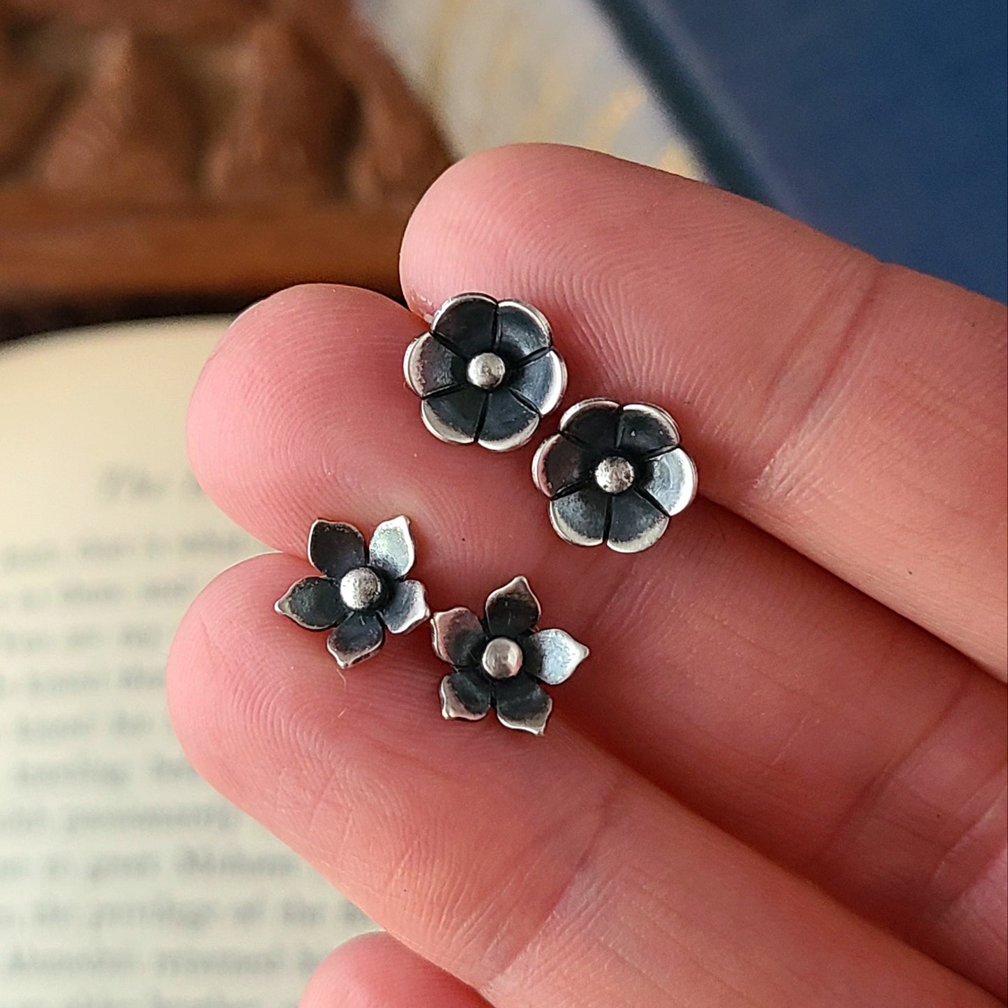two pairs of silver flower studs held between fingers over an open book