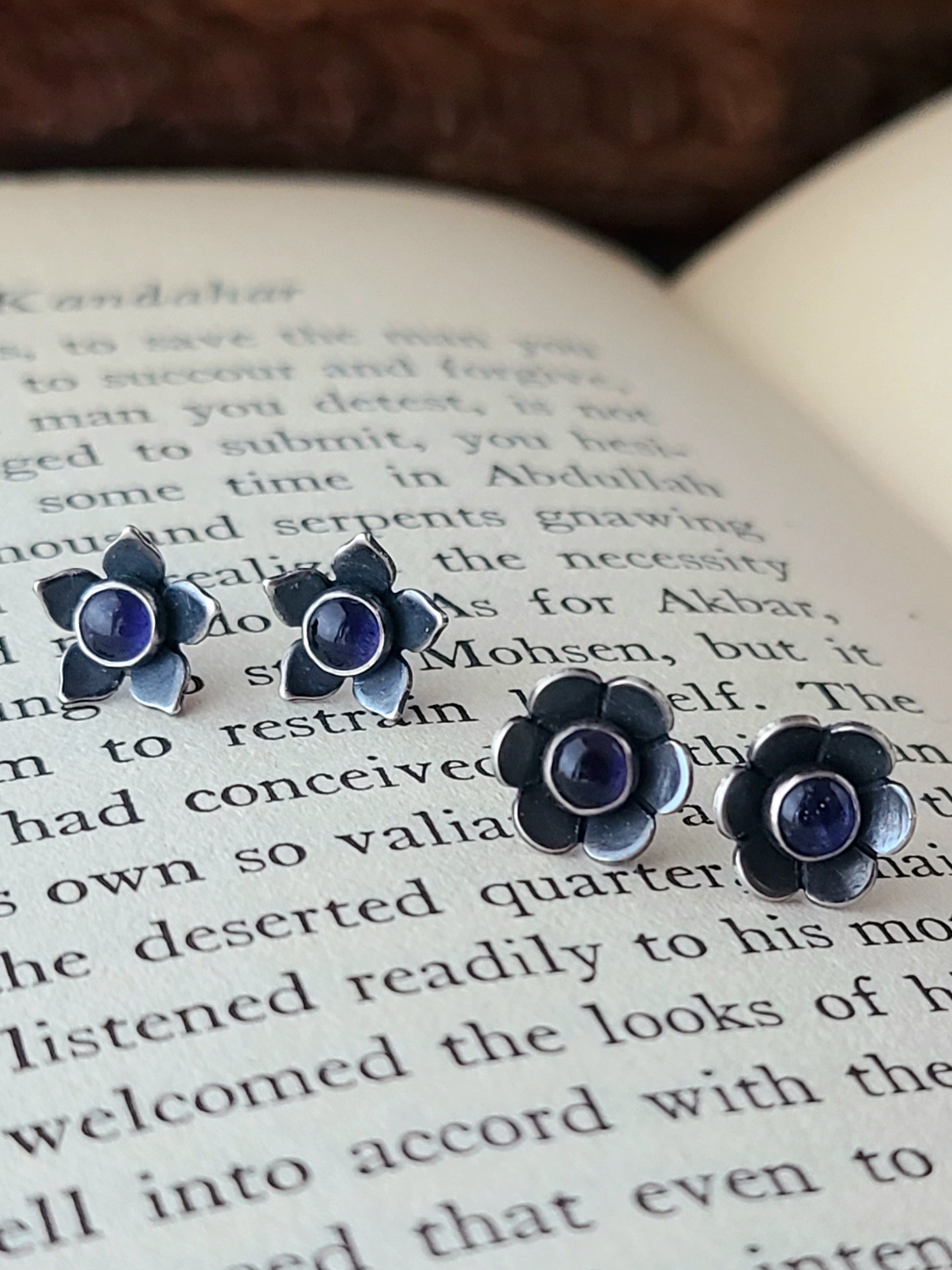 two pairs of silver flower studs with dark blue gemstones displayed on an open ook