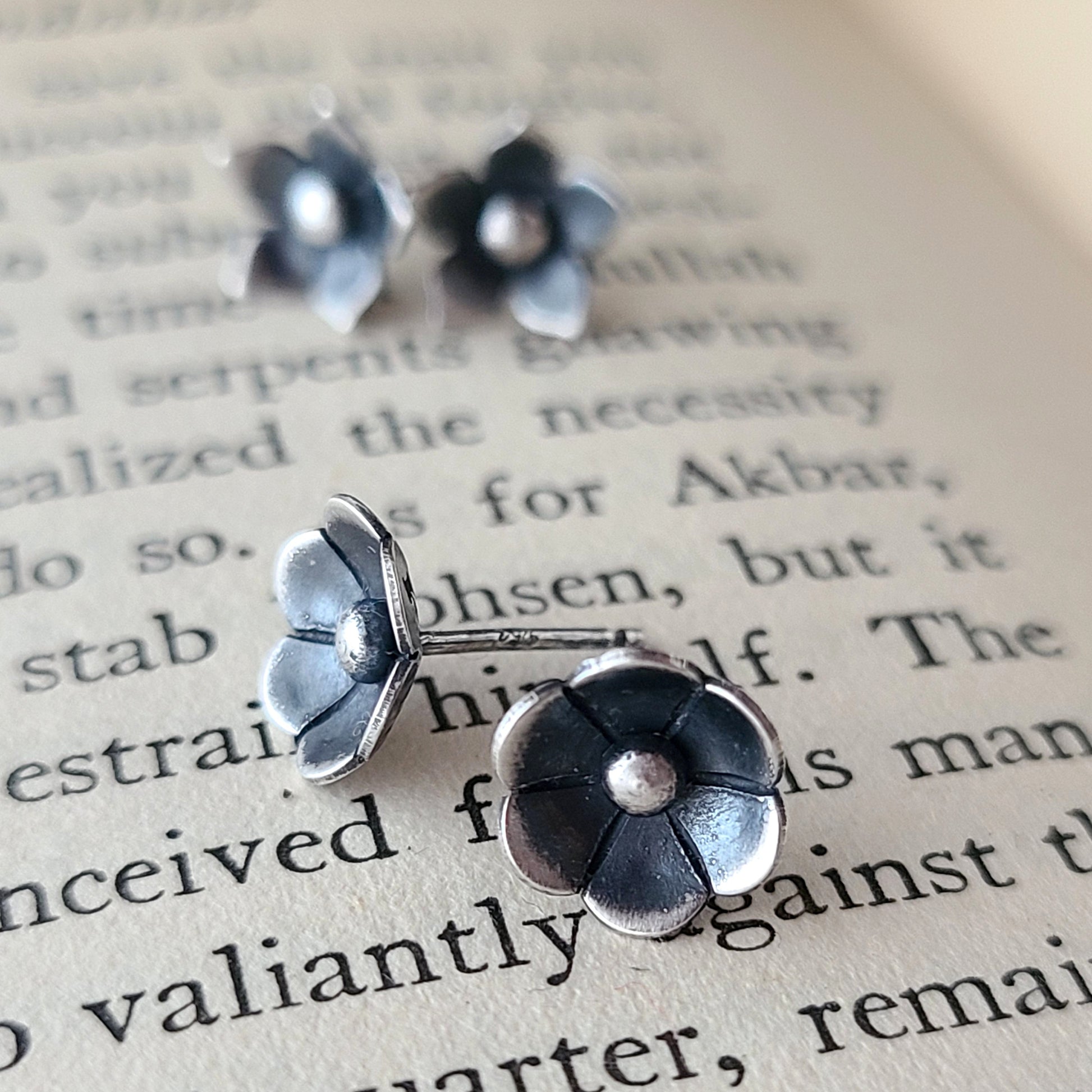 A pair of sterling silver flower stud earrings placed on an open book page.