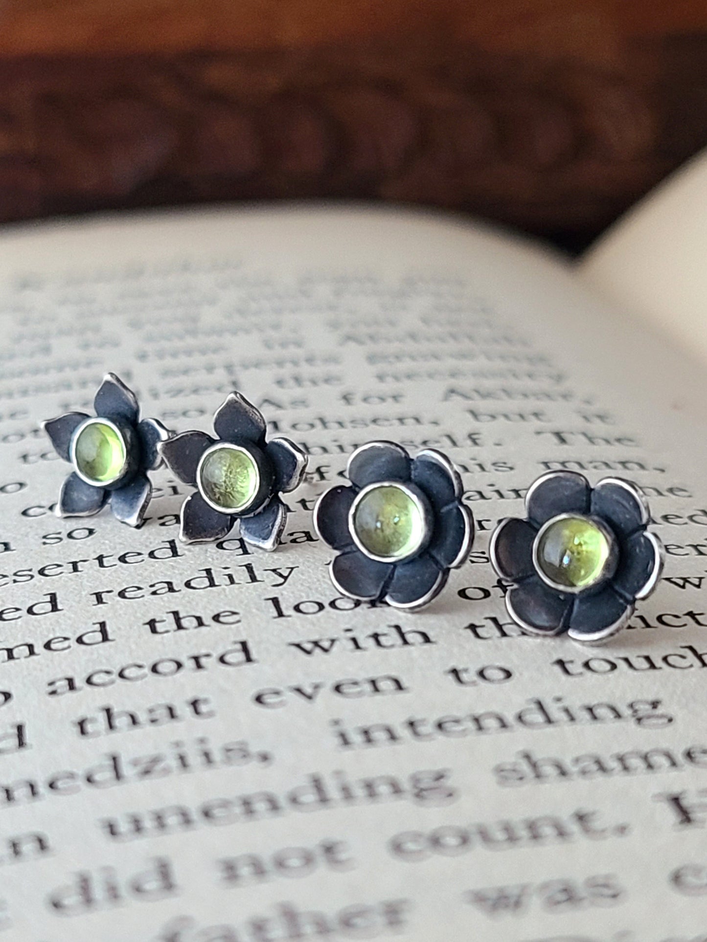 two pairs of silver flower stud earrings with light green gemstones on an open book