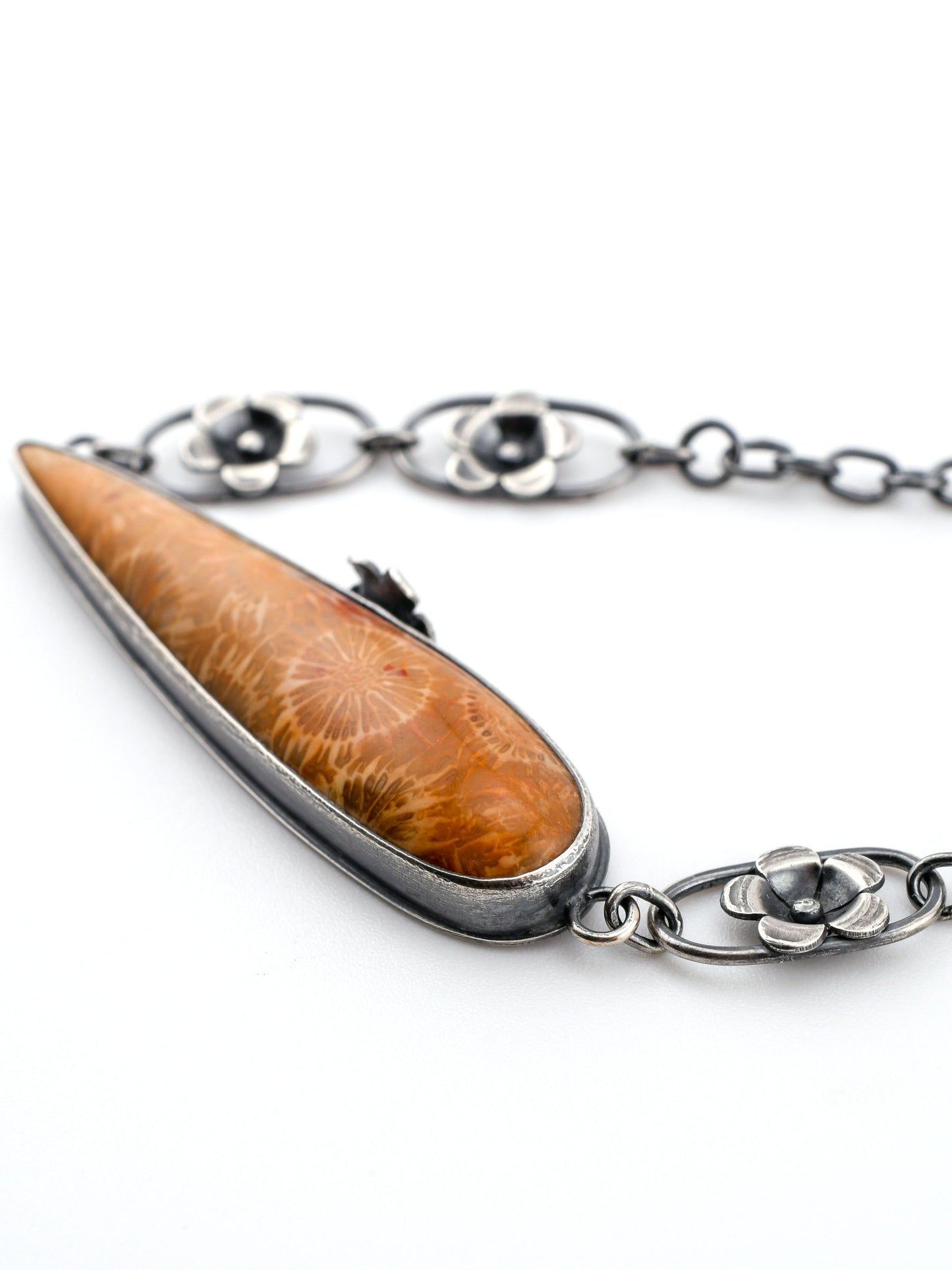 Closeup of long fossil coral pendant and silver flower chain on a white background