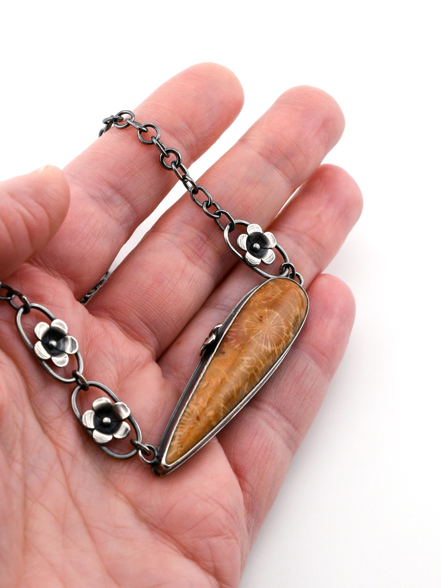 Hand holding a necklace with a large pendant on a white background