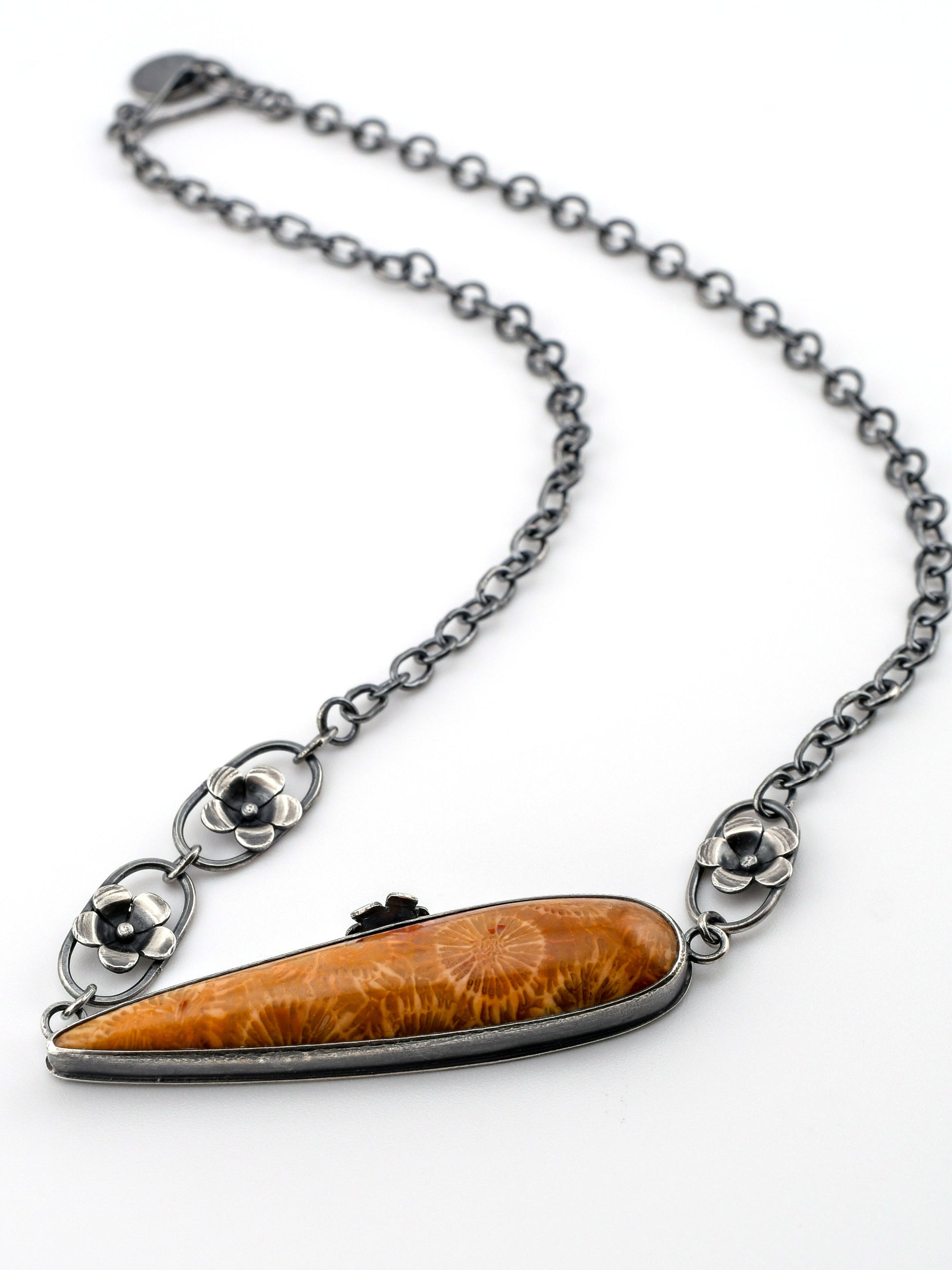 Necklace with unique fossil coral pendant and silver flower chain elements on a white background
