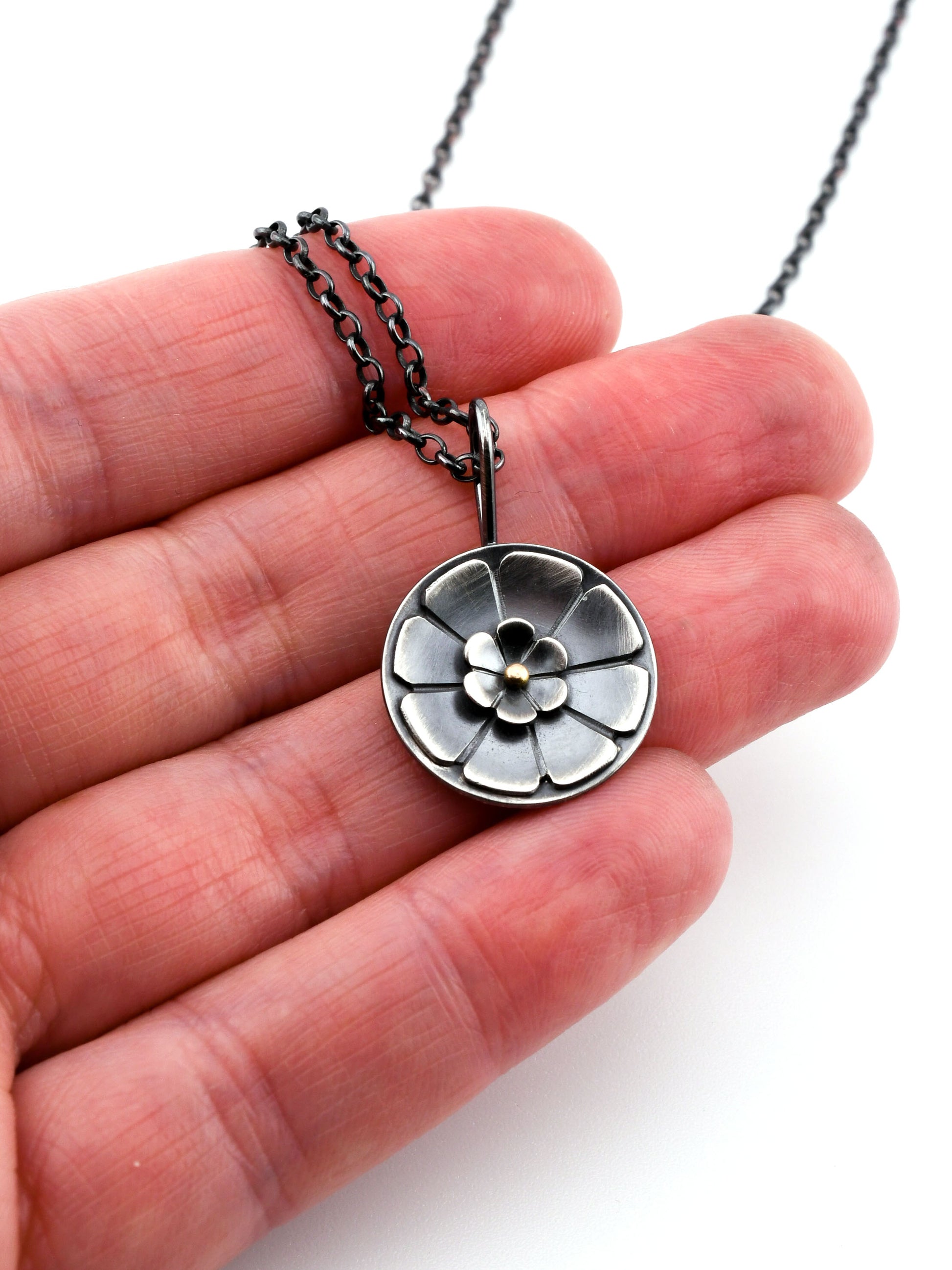 Silver floral pendant necklace held in a hand against a white background