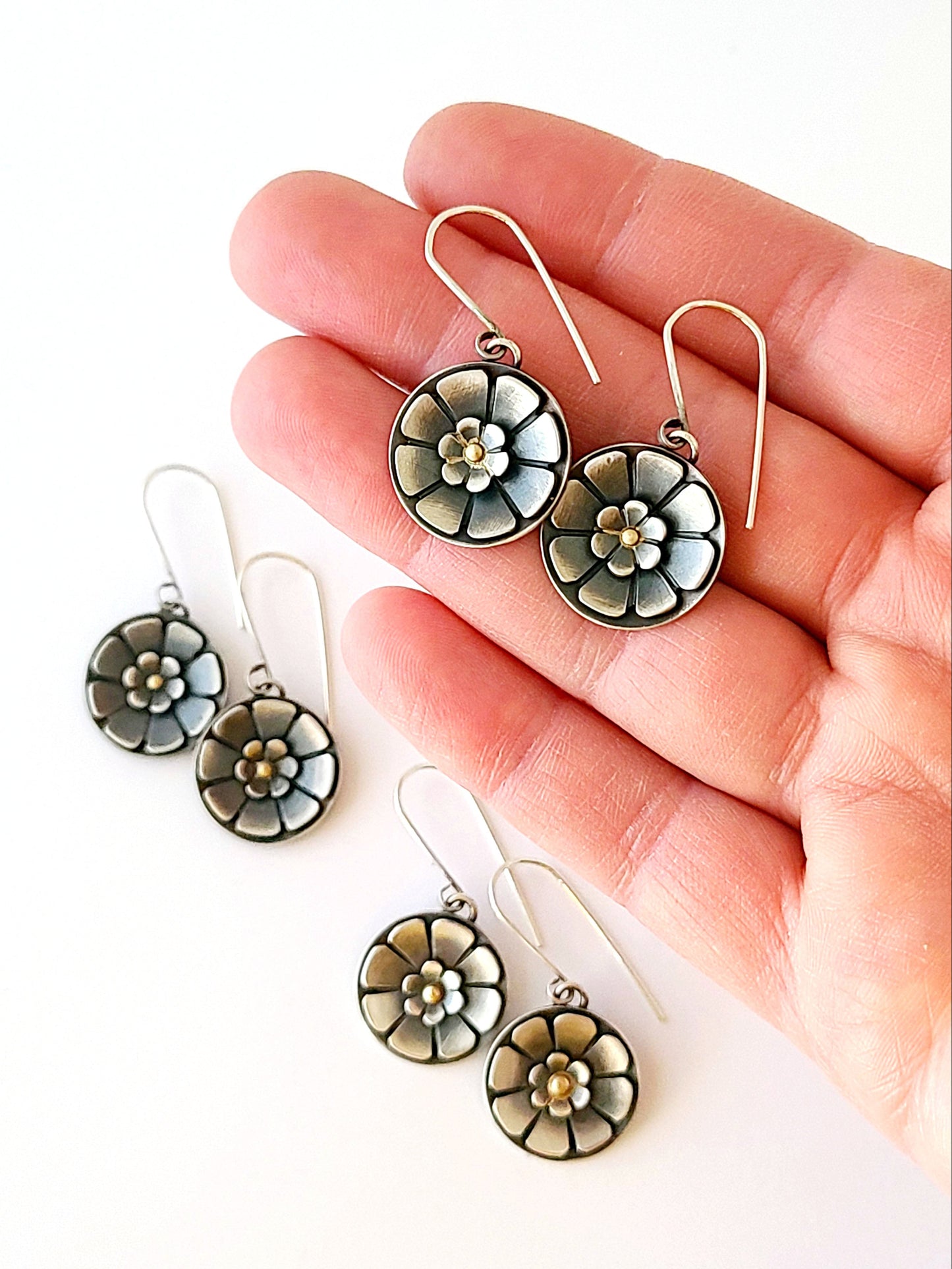 flower earrings held in a hand over a white background with two more pairs of flower earrings