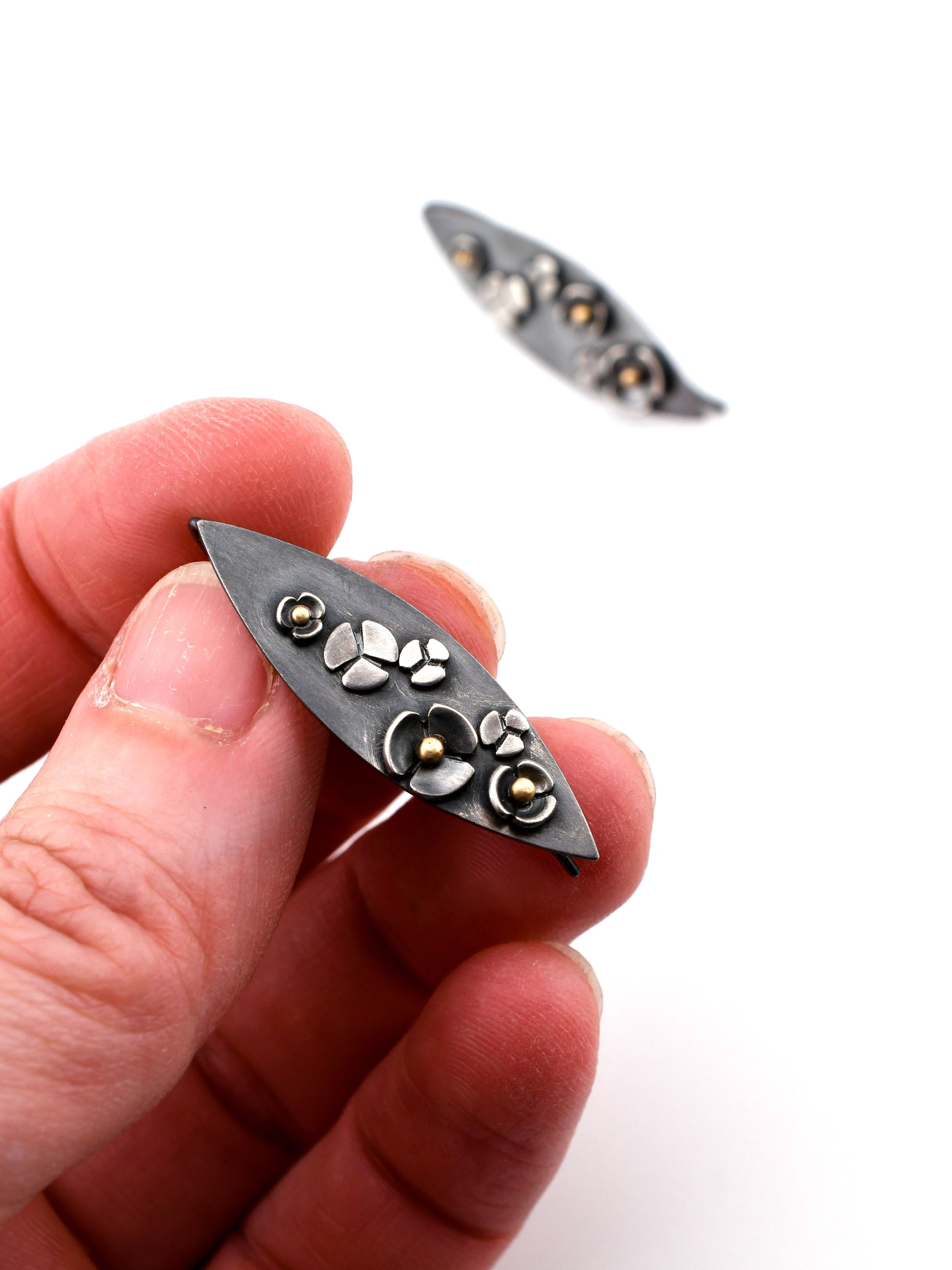 Hand holding a blackened silver earring with flowers and gold accents on a white background