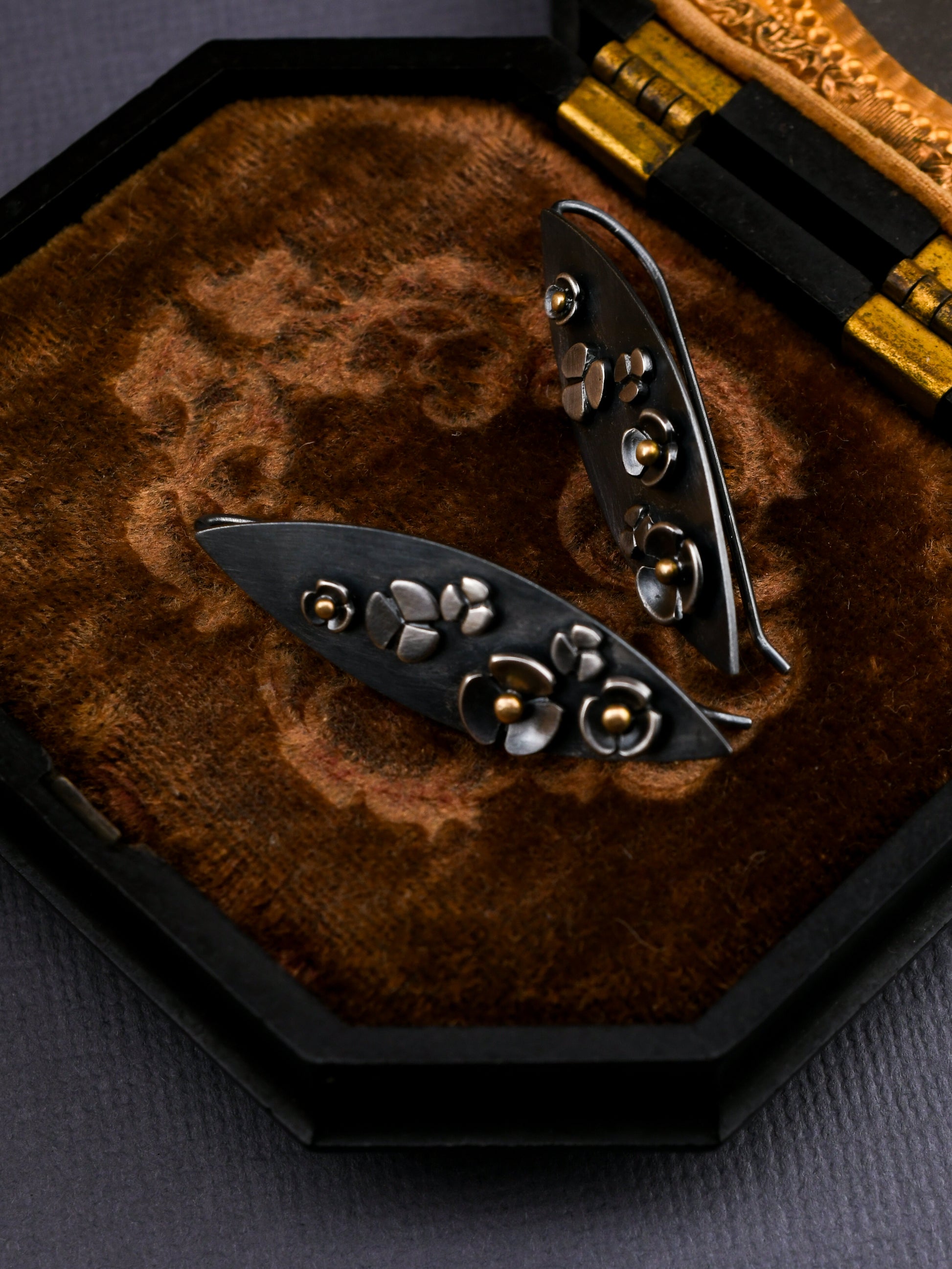 Blackened silver earrings with floral details on a textured surface
