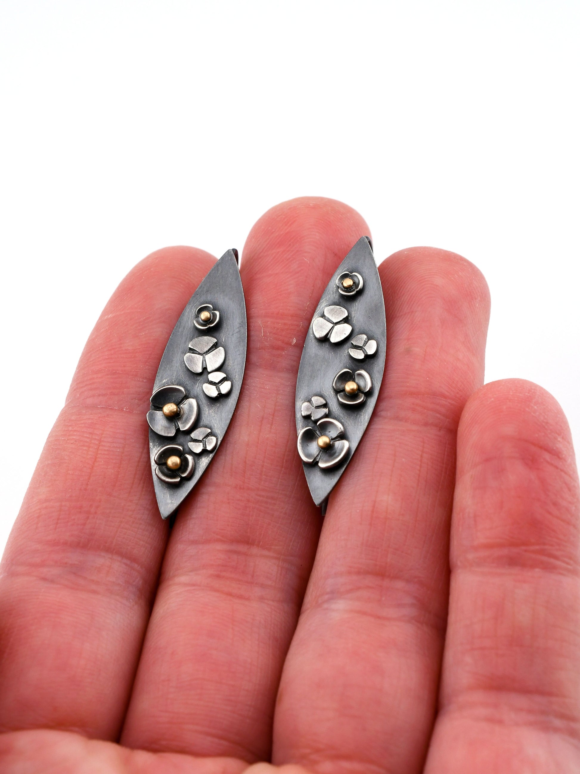 Silver floral earrings held between fingers on a white background